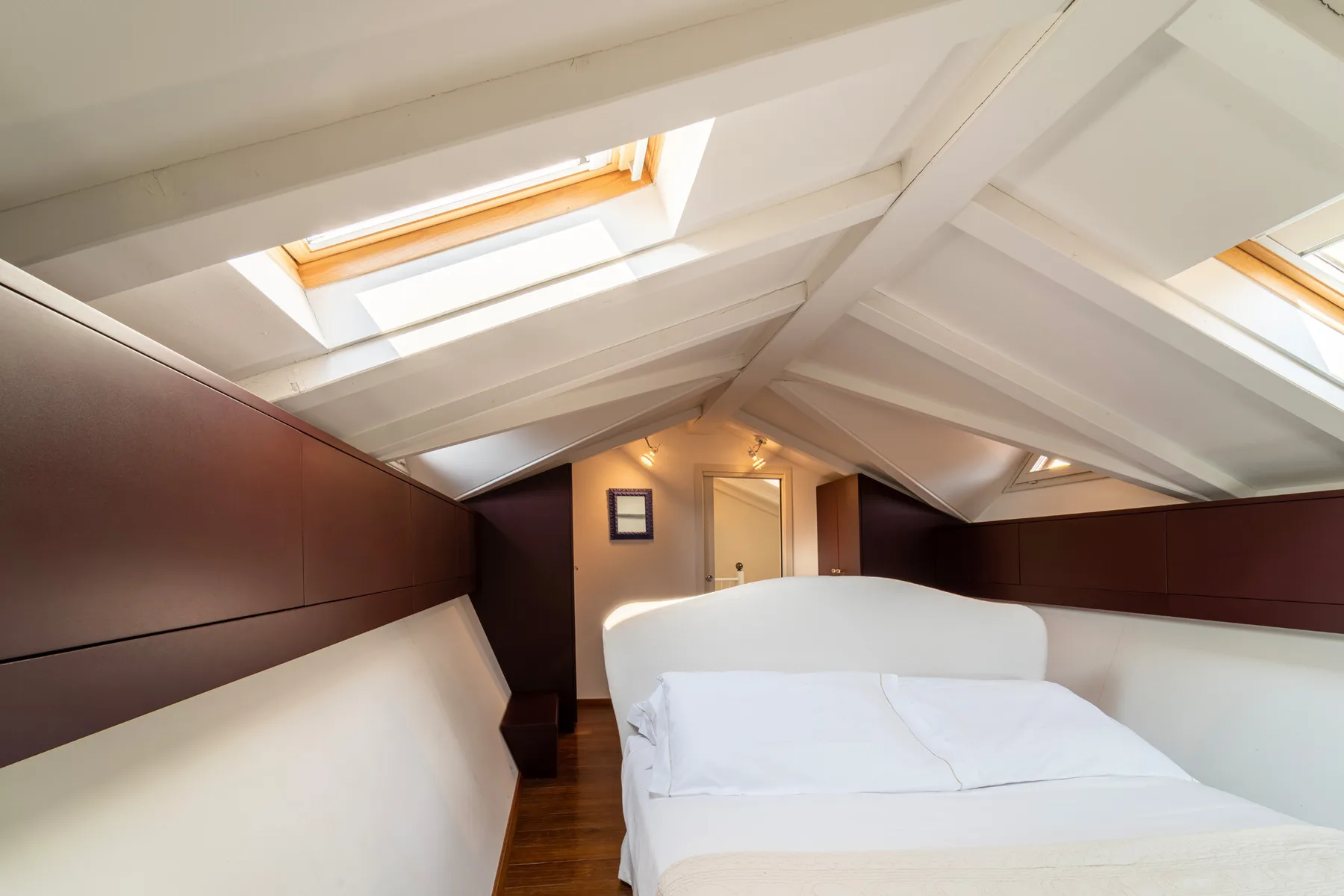 Un dormitorio con una cama bajo un techo inclinado y tragaluces.