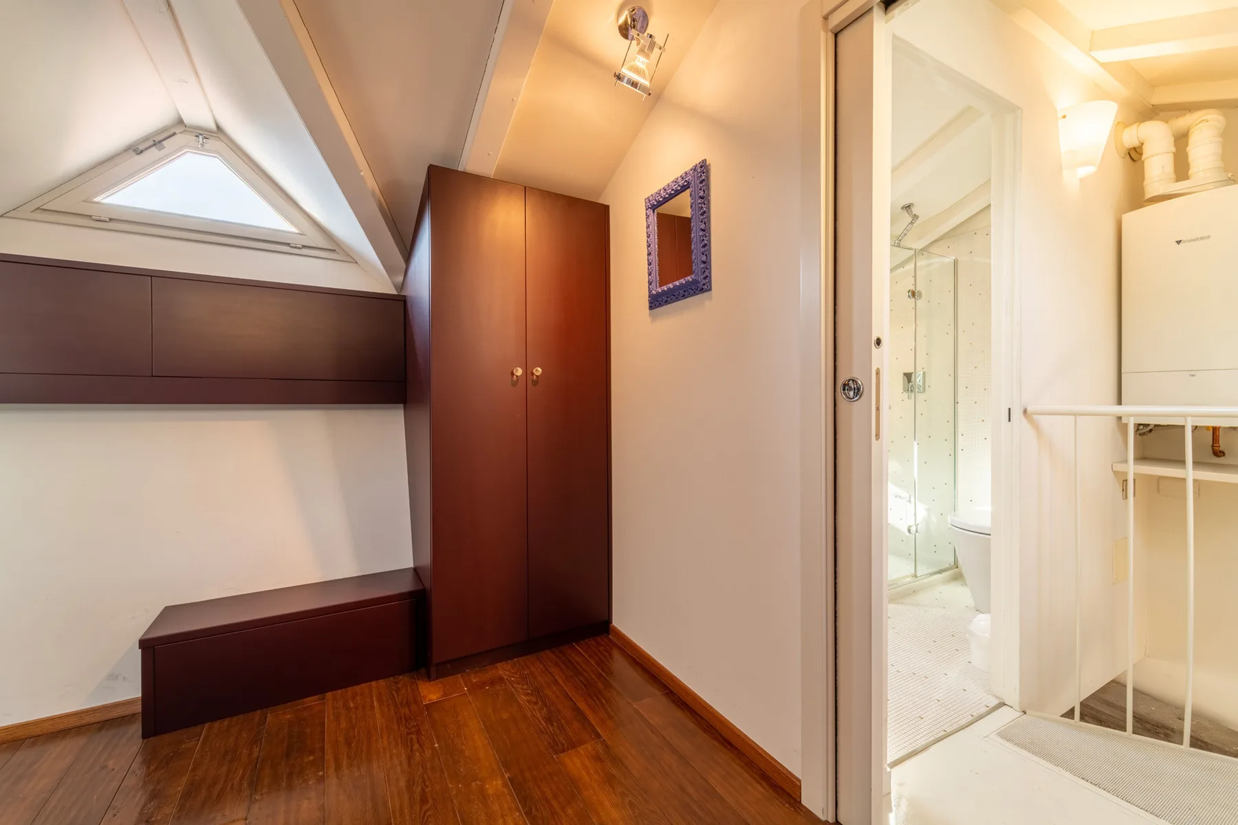 Un pequeño dormitorio abuhardillado con un armario de madera y una puerta al baño.