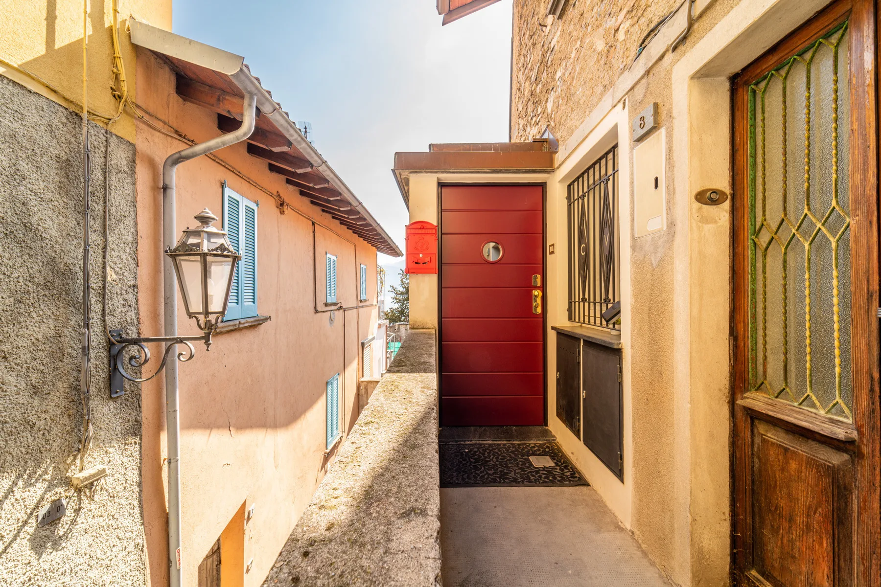 Un pasaje exterior estrecho transcurre entre edificios hacia una puerta roja.