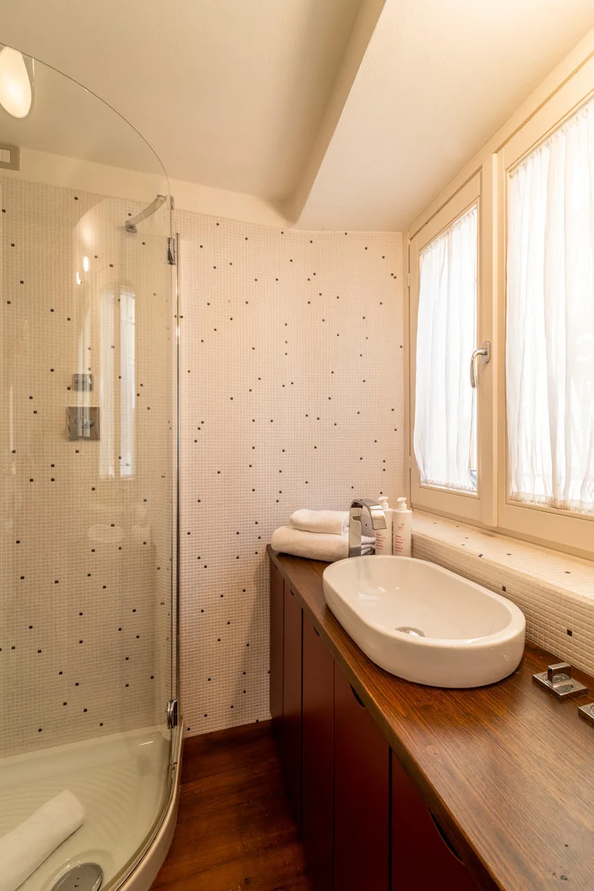 Un baño con una ducha de vidrio y un lavabo bajo ventanas luminosas.