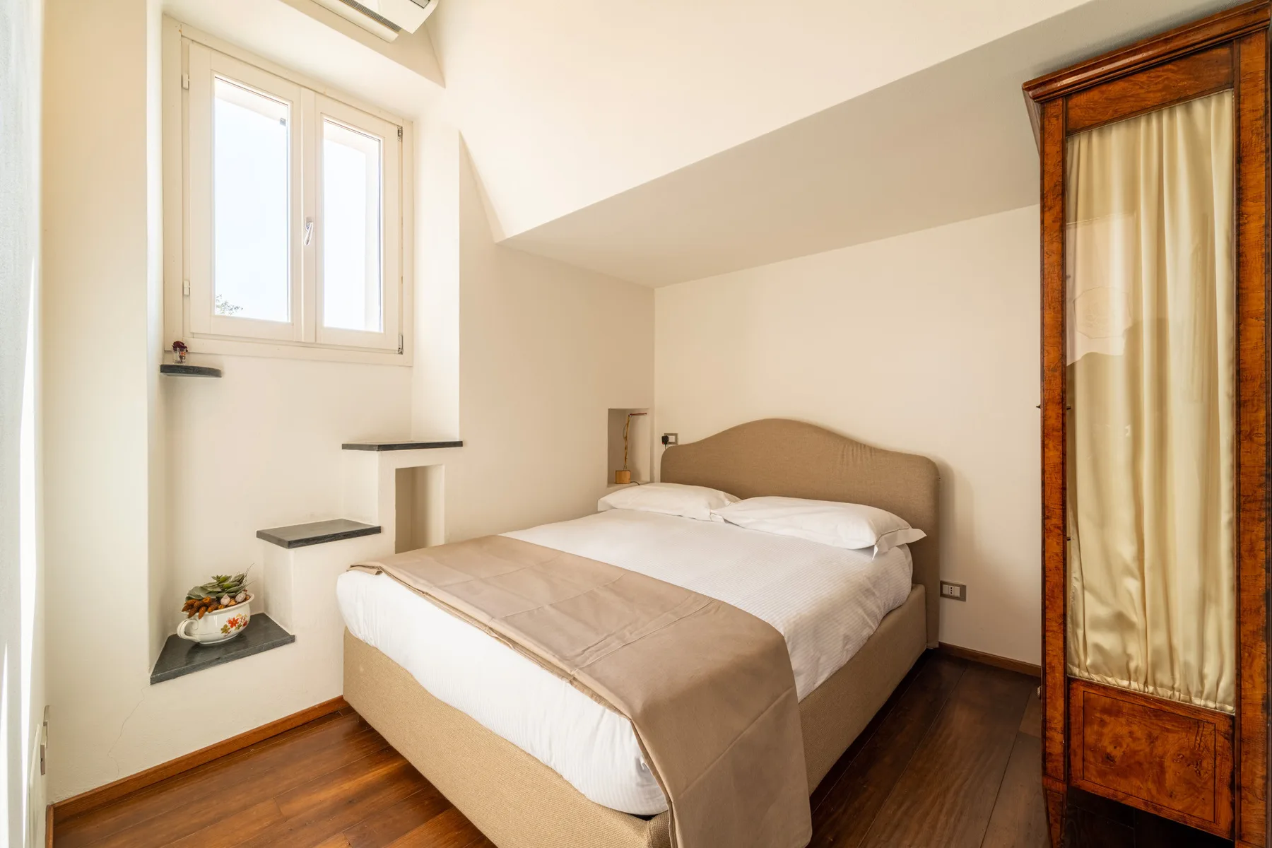 Un dormitorio con una cama bien tendida y una ventana al lado.