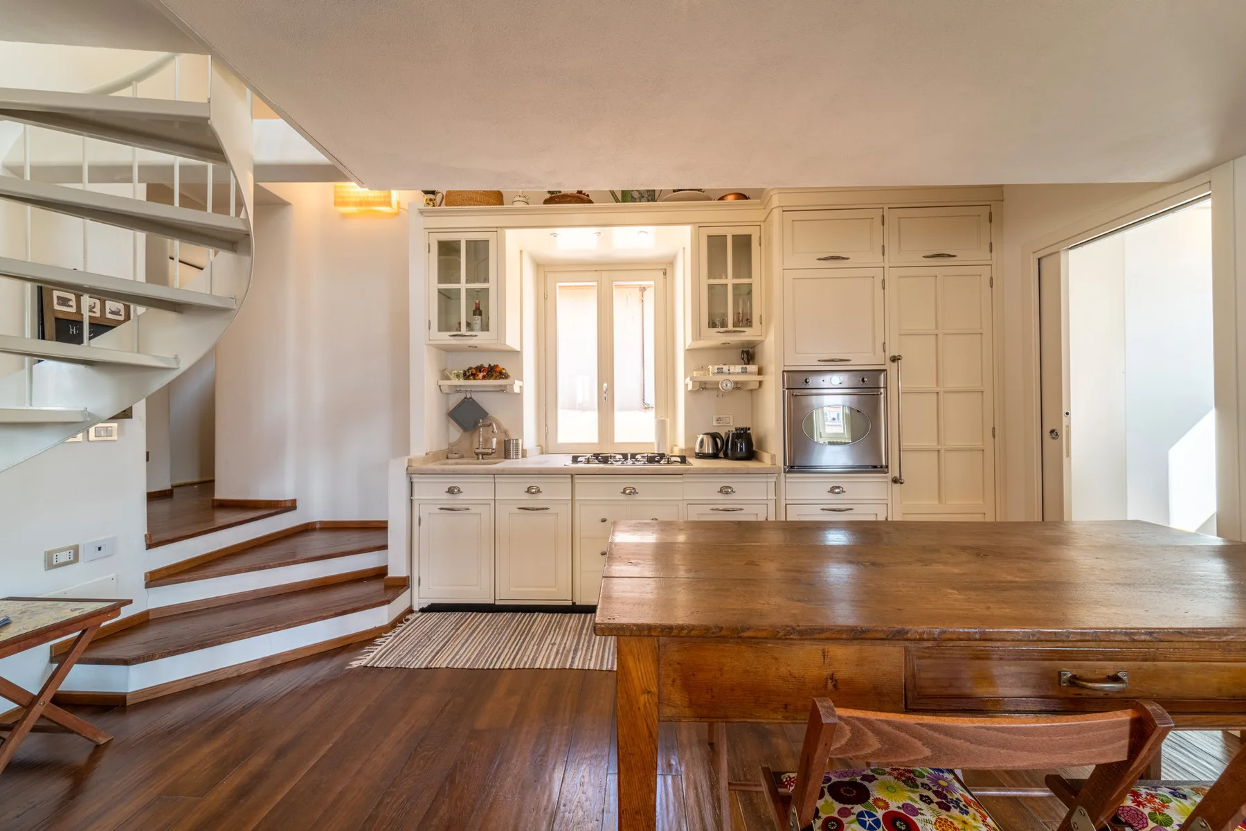 Una cocina luminosa con muebles claros, una isla central y una escalera.