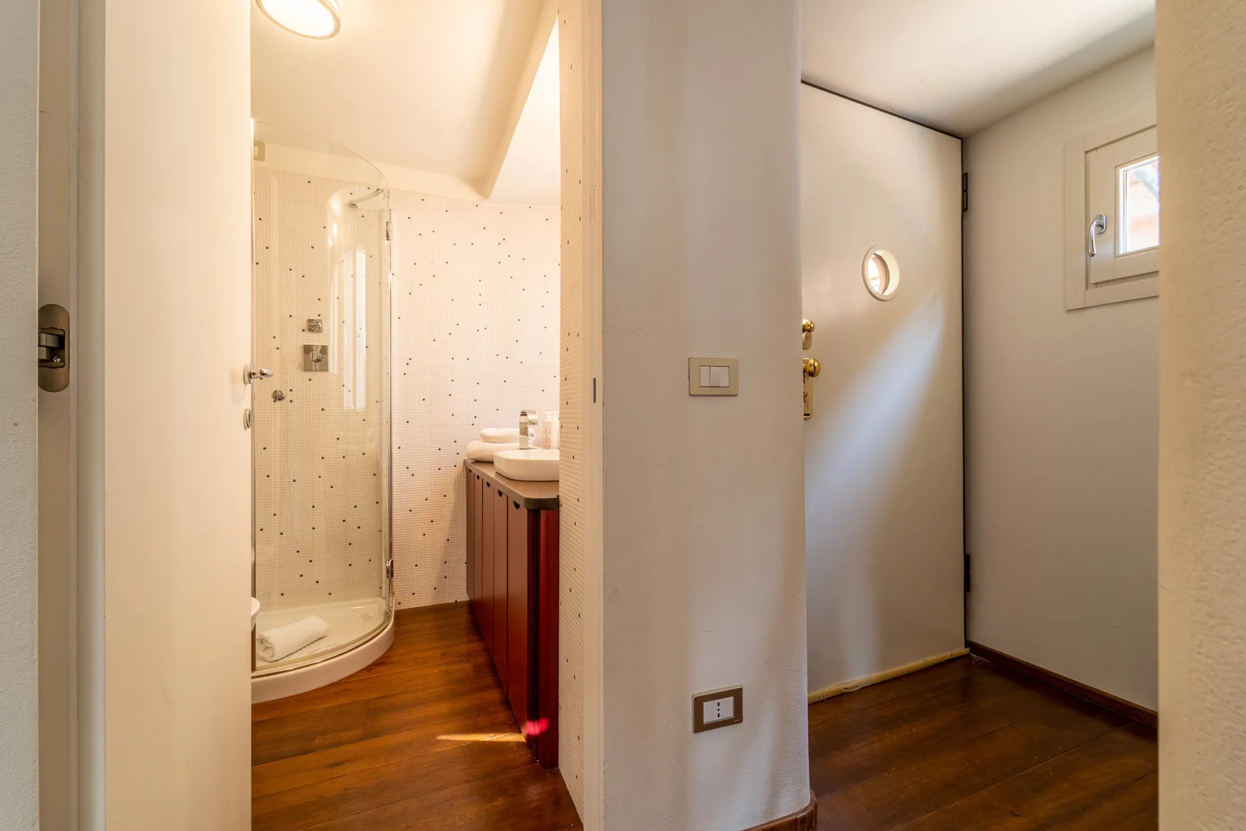 Un baño con ducha de vidrio y lavabo junto a una pequeña zona de entrada.
