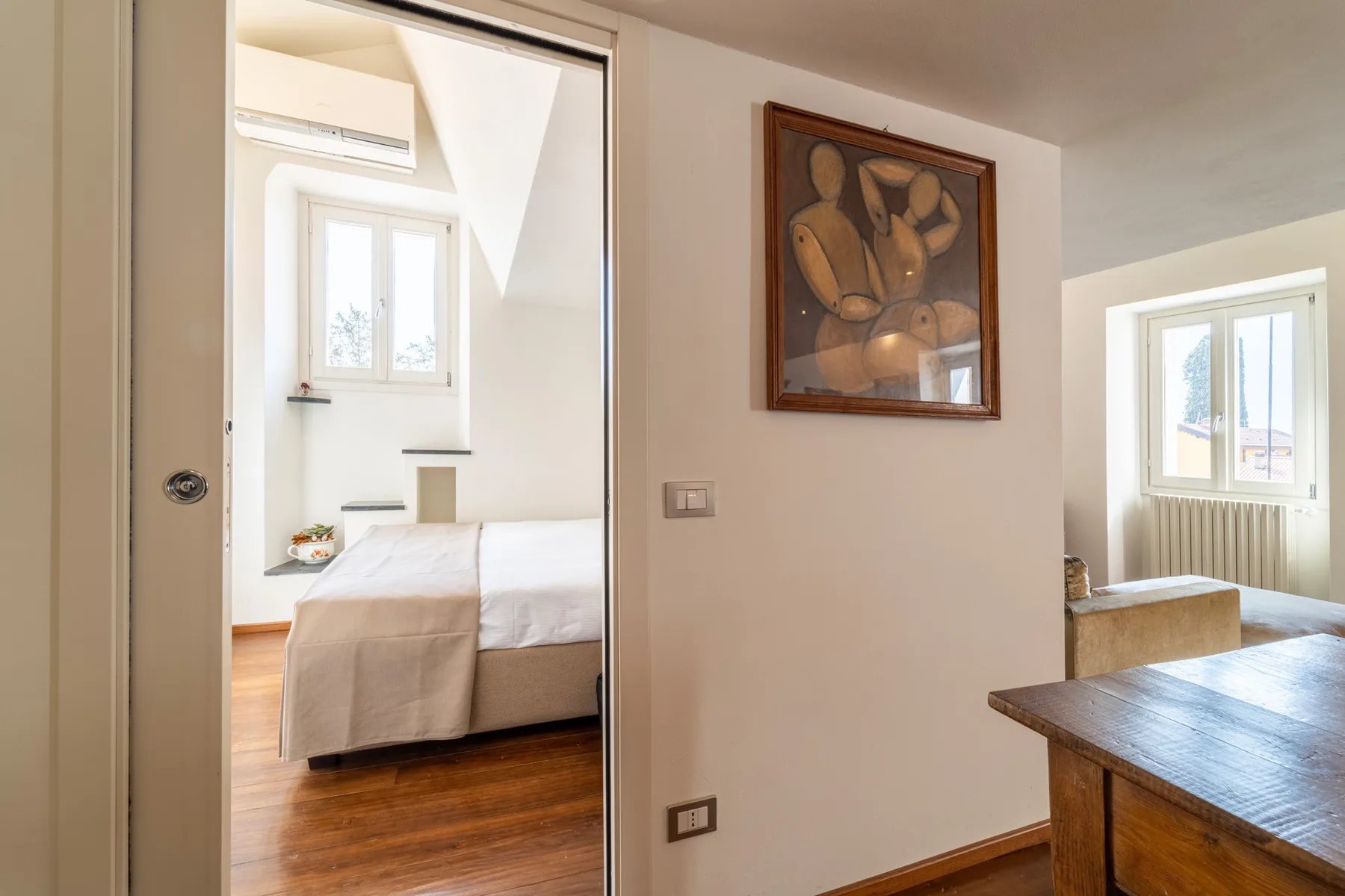 Un dormitorio luminoso se abre a una zona de estar, con un cuadro en la pared.