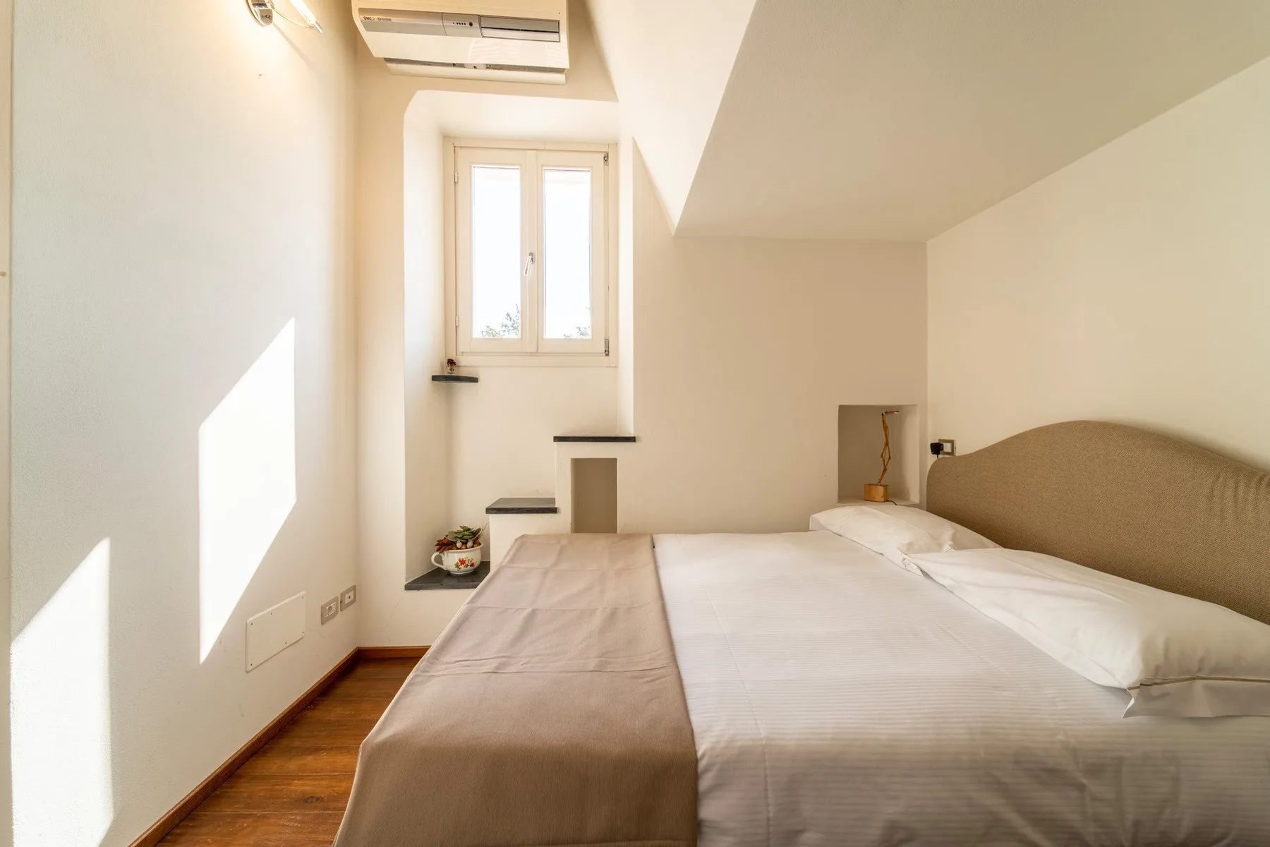 Un dormitorio luminoso con una cama bajo un techo inclinado y una ventana.