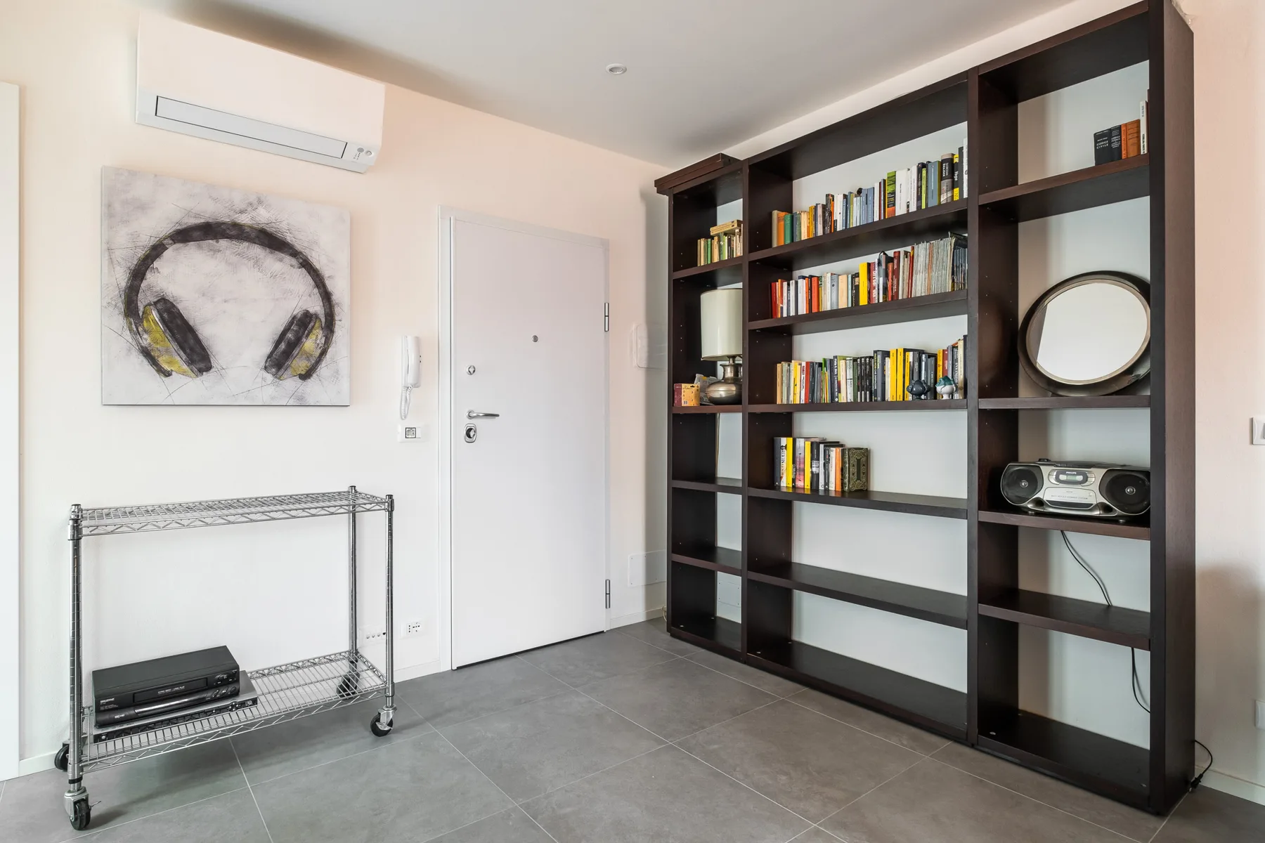 A room with a tall dark bookcase, wall art, and a metal shelving cart.