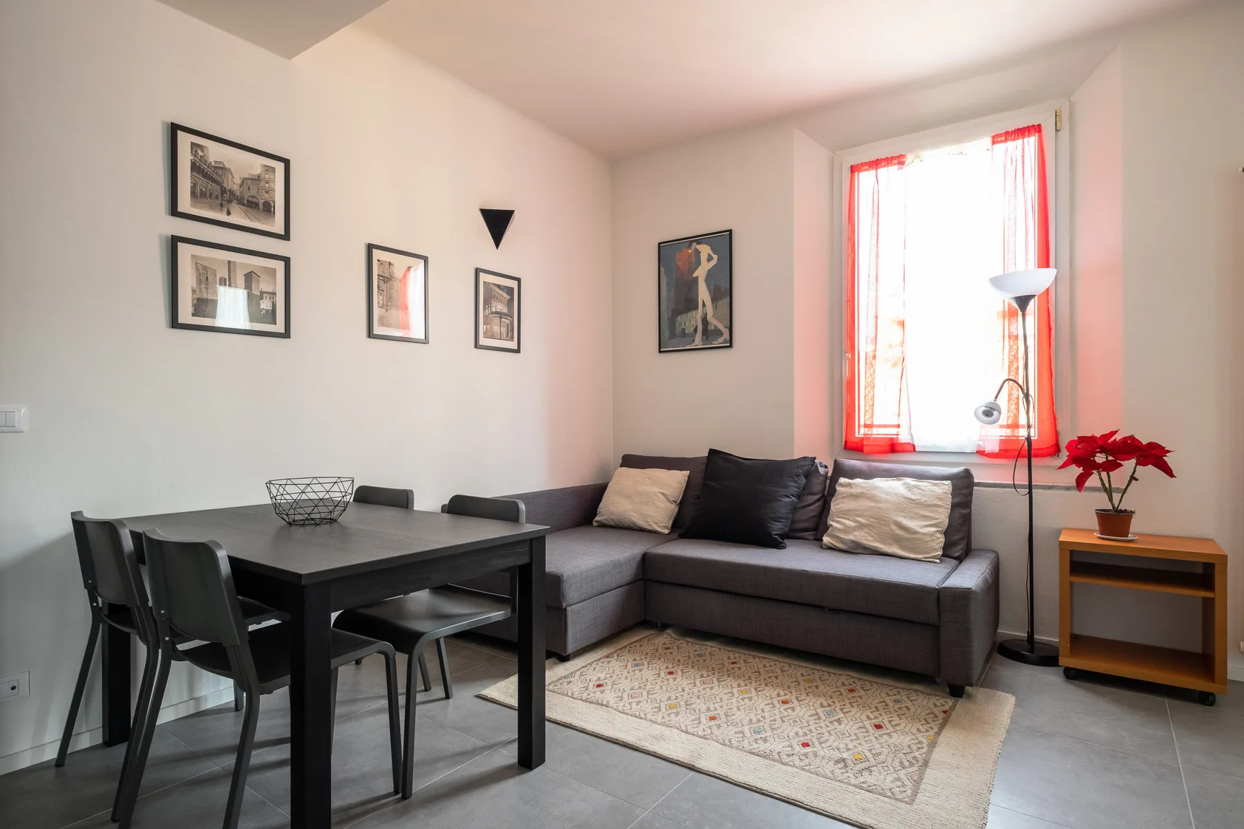 Sala de estar con zona de asientos gris, mesa de comedor y ventana luminosa.