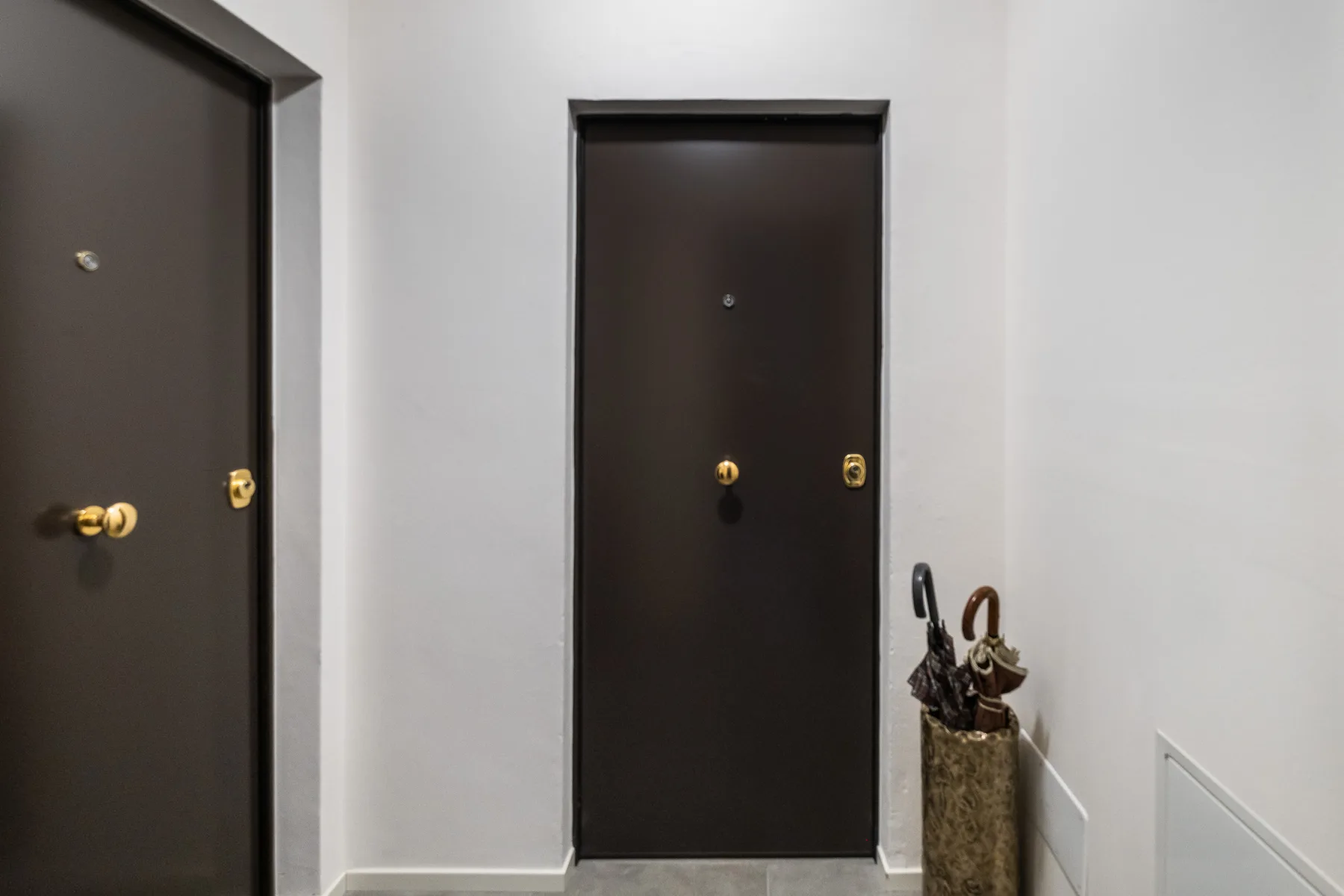 Un pasillo interior con puertas oscuras y un paragüero.
