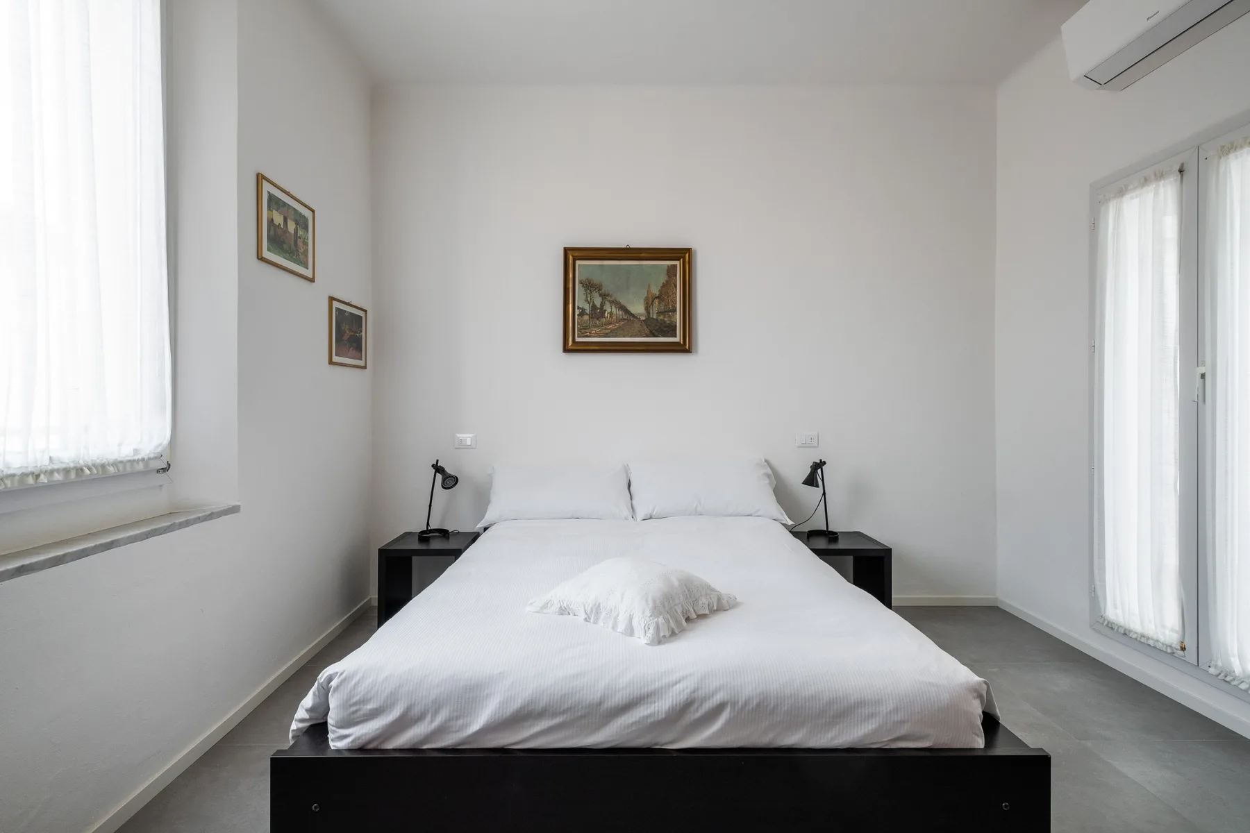 Un dormitorio luminoso con una cama bien arreglada y cuadros en las paredes.