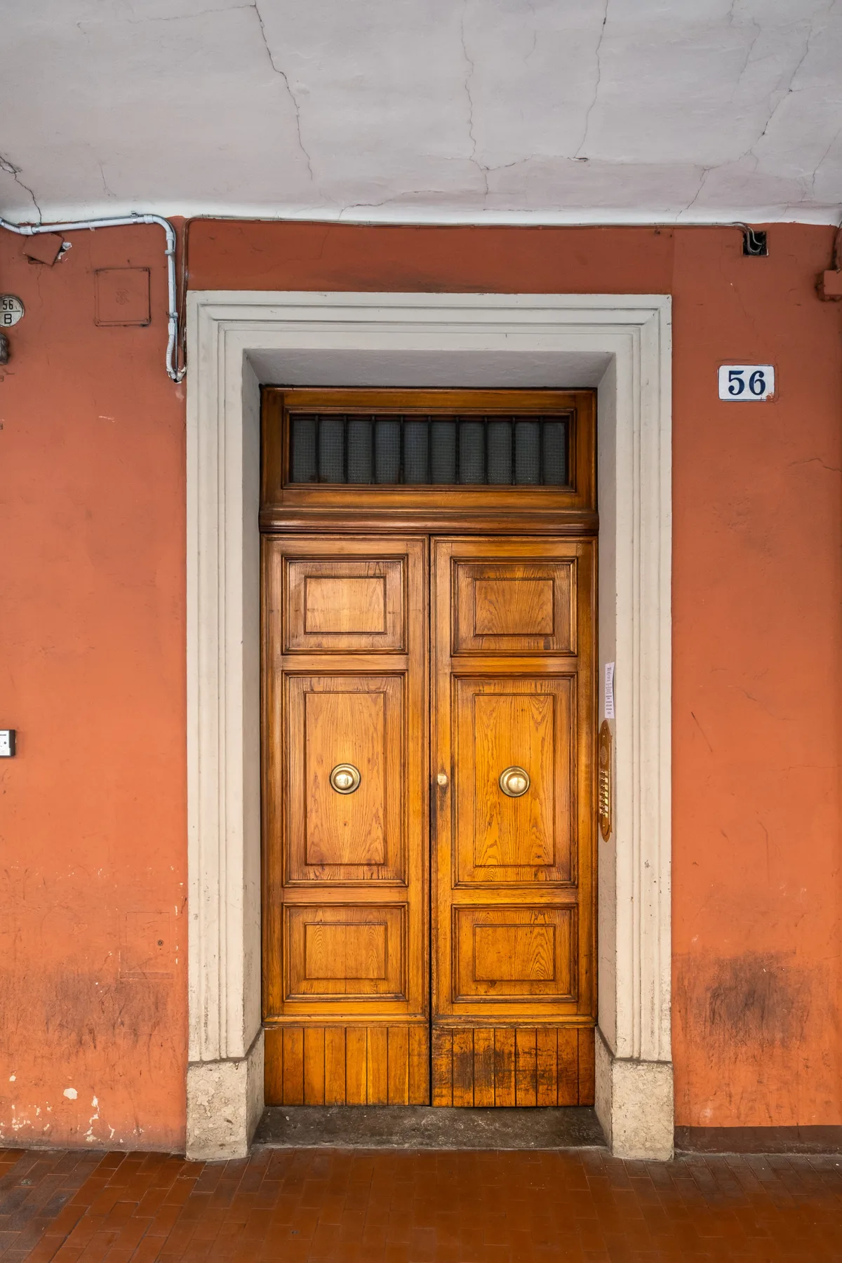 Una puerta doble de madera con paneles de vidrio está en una pared exterior naranja.
