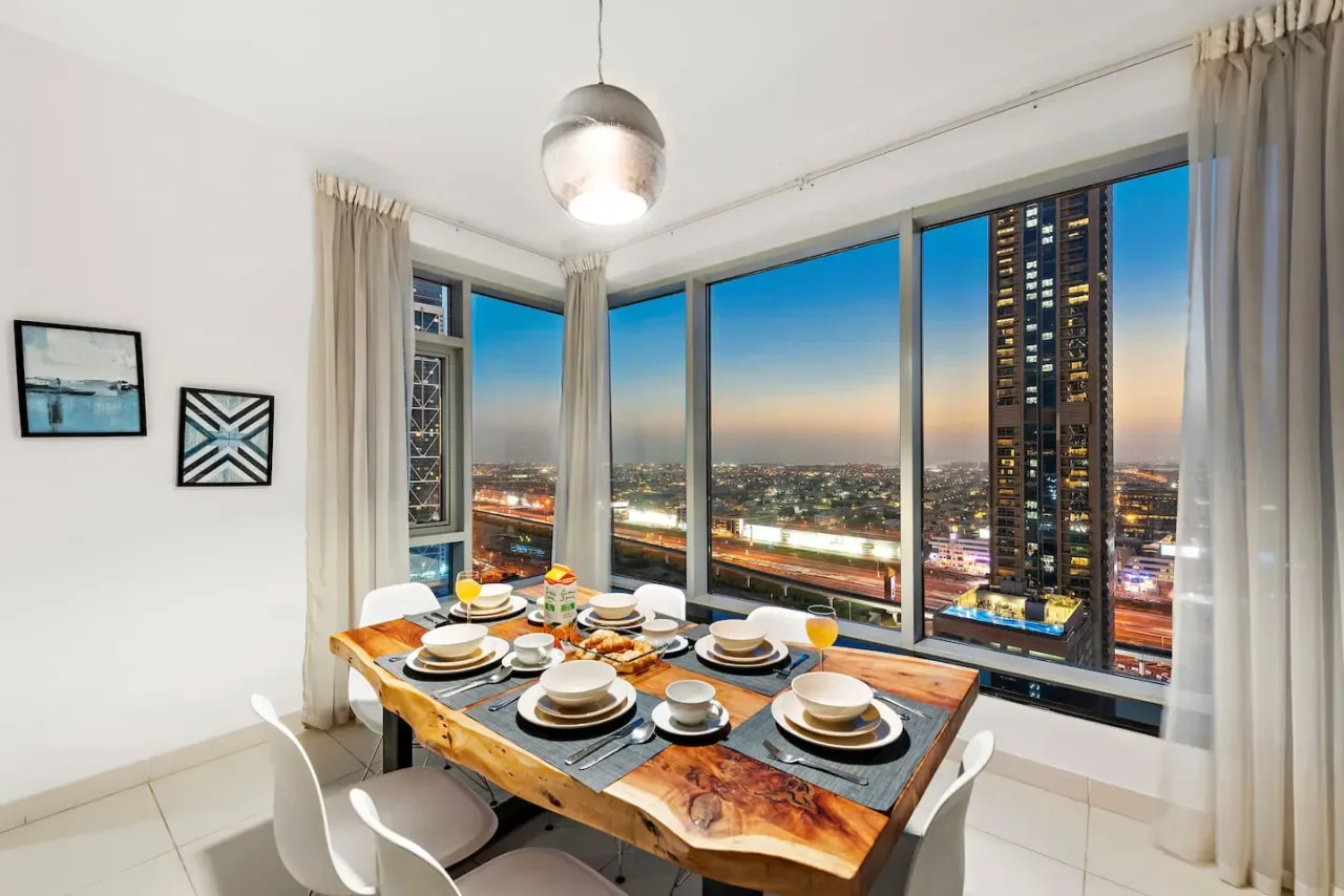 Comedor con una mesa de madera junto a ventanales con vistas a la ciudad.