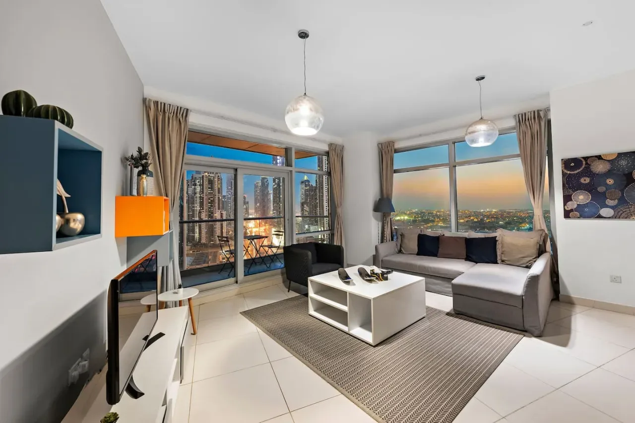 Una sala luminosa con asientos, una mesa de centro y grandes ventanas con vistas a la ciudad.