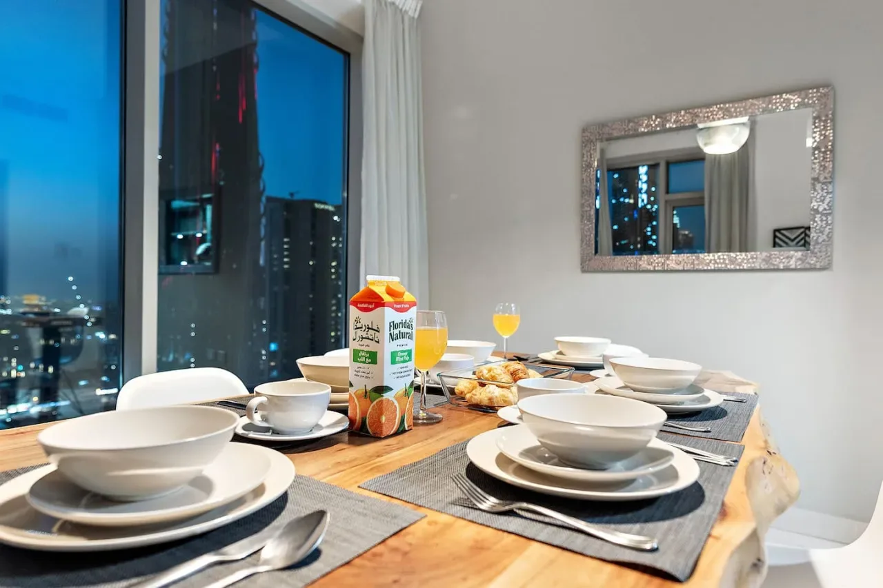 Una mesa de comedor con puestos servidos está junto a una gran ventana con vistas a las luces de la ciudad.