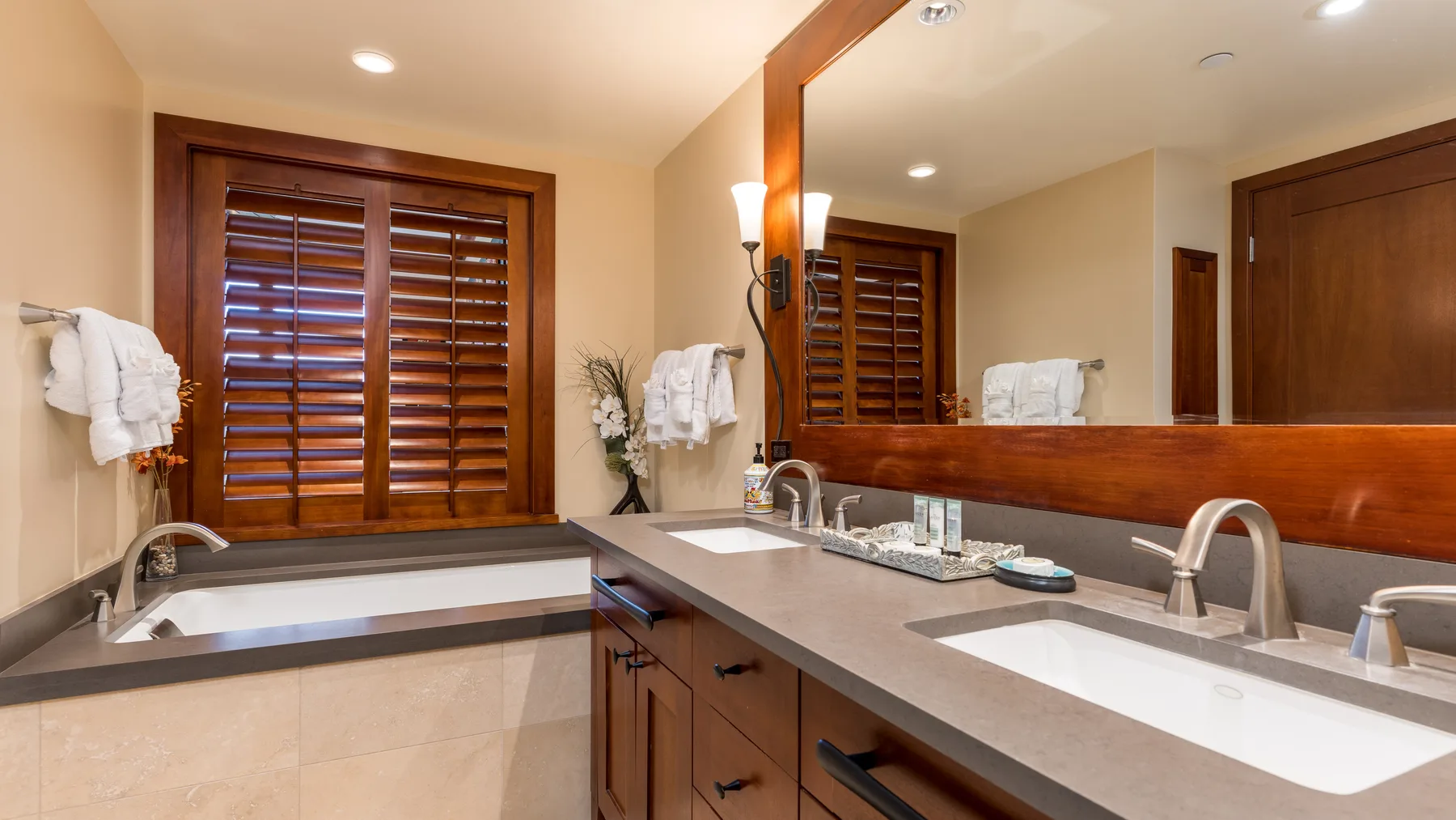 Un tocador de baño con un espejo amplio y una bañera junto a una ventana con contraventanas.