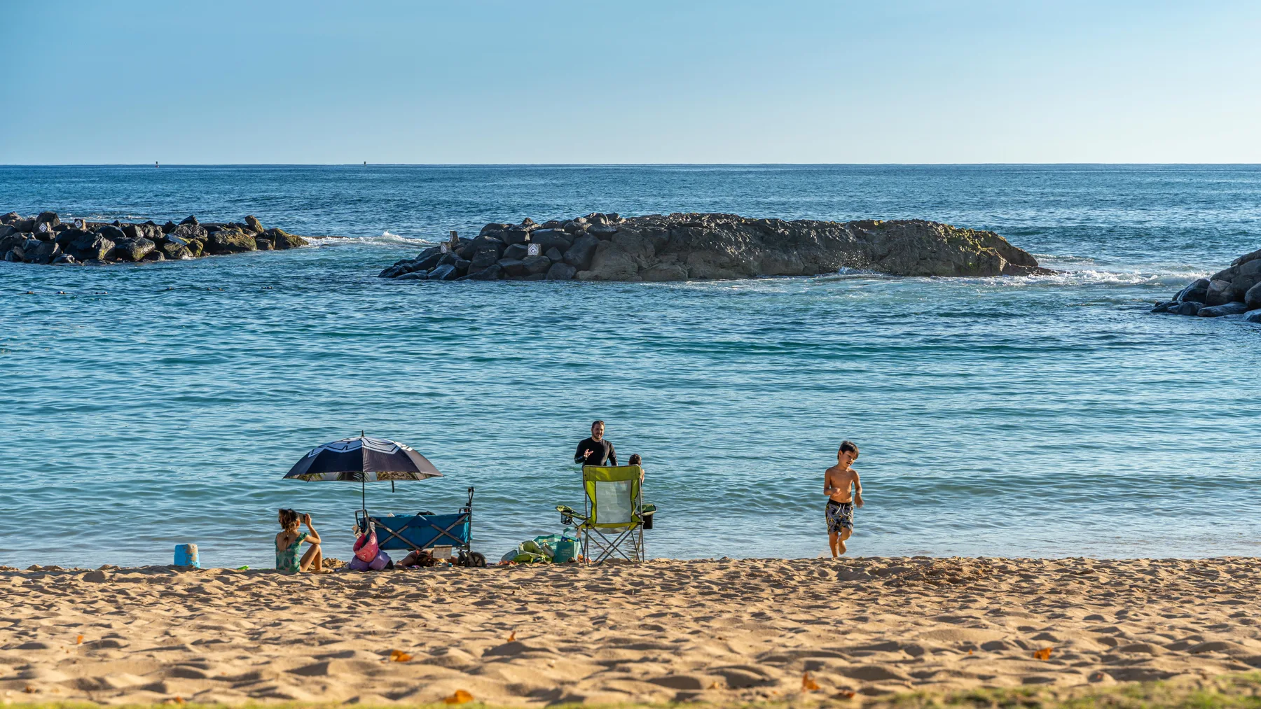 Una playa de arena se encuentra con aguas azules tranquilas, con personas junto a la orilla.