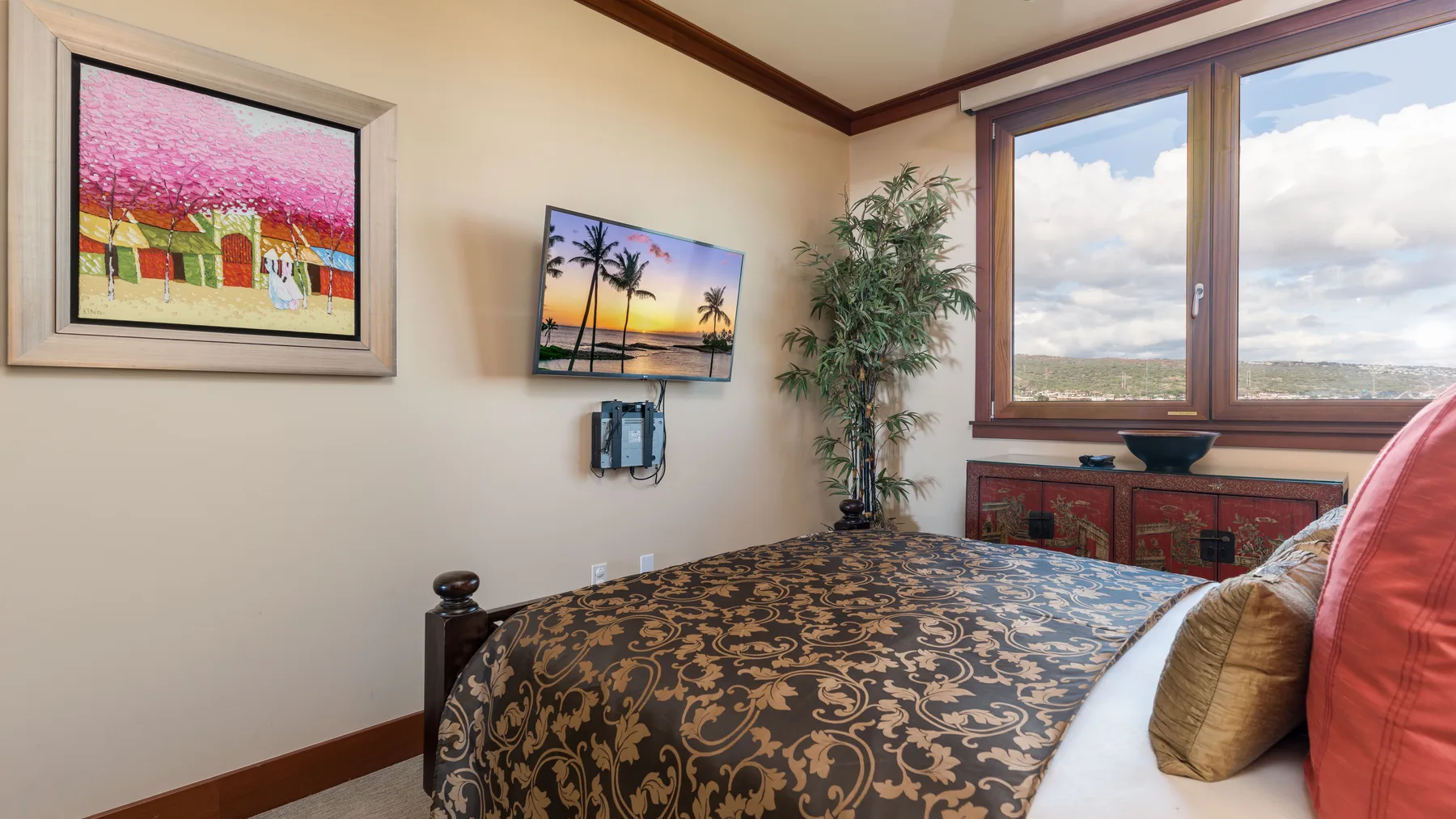 Dormitorio con una colcha estampada, un televisor en la pared y ventanas grandes.