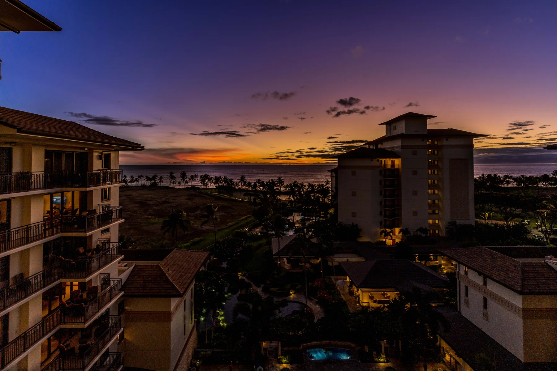 Edificios y palmeras enmarcan una puesta de sol colorida sobre el agua.