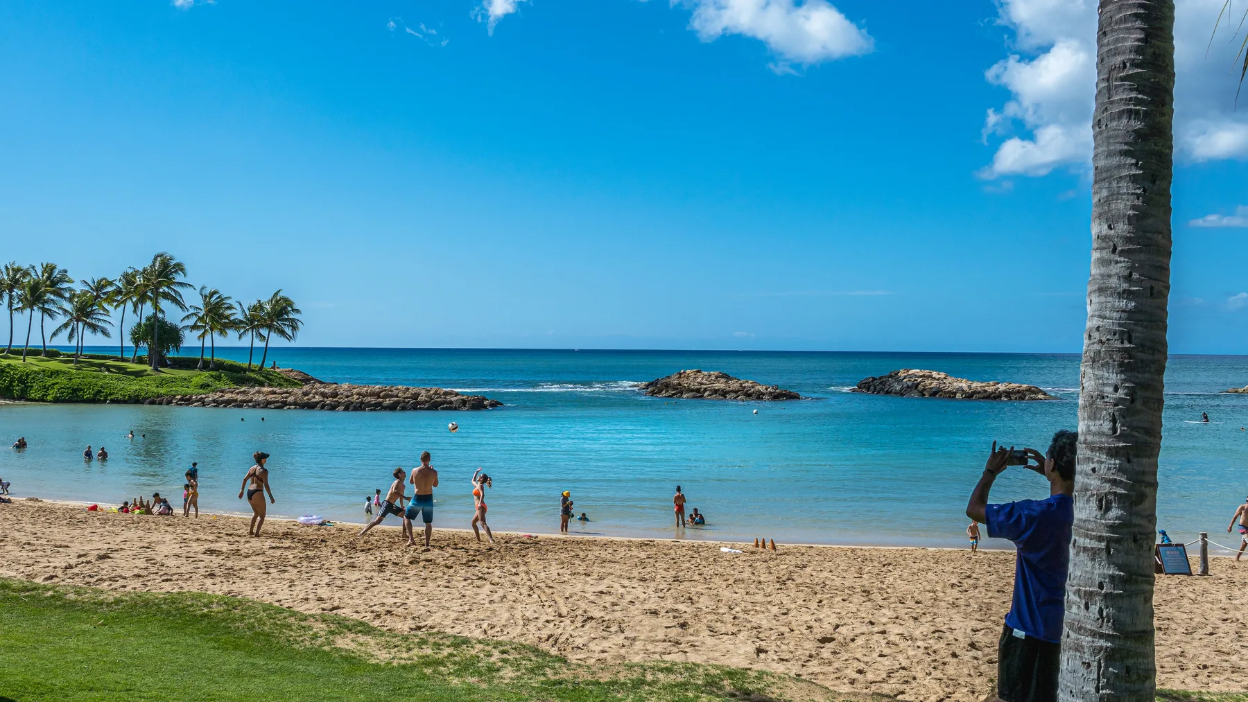 Una playa de arena con personas nadando en el agua azul y tranquila.