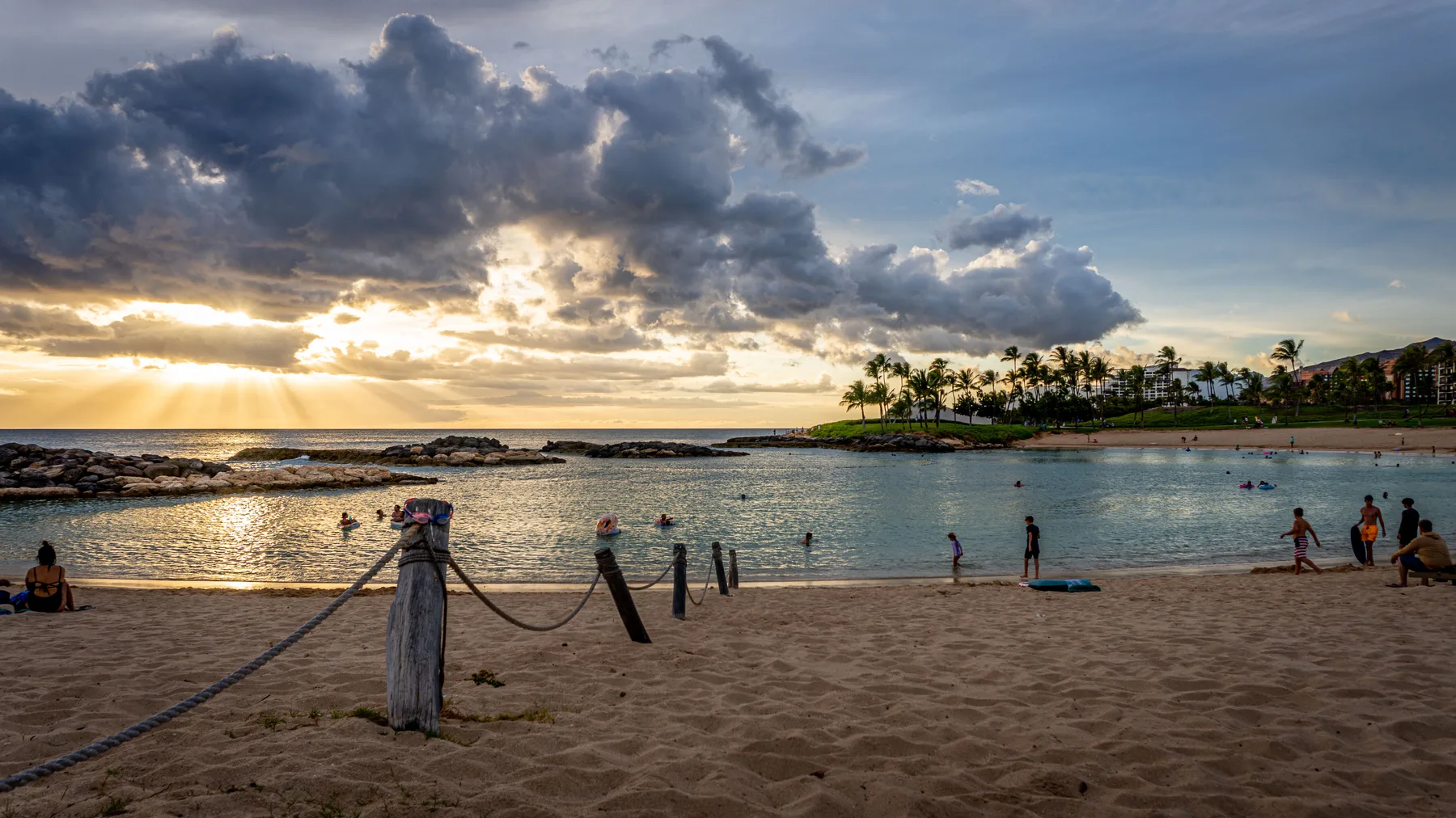 Una playa de arena junto a aguas tranquilas al atardecer, con personas en la orilla.