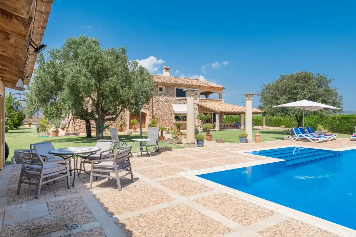 Una piscina y asientos en el patio están junto a una casa de piedra y un jardín.