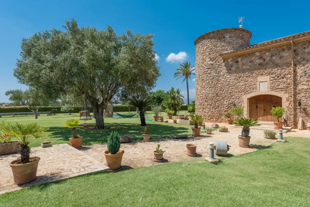 Un edificio de piedra se alza junto a un jardín con plantas en macetas.