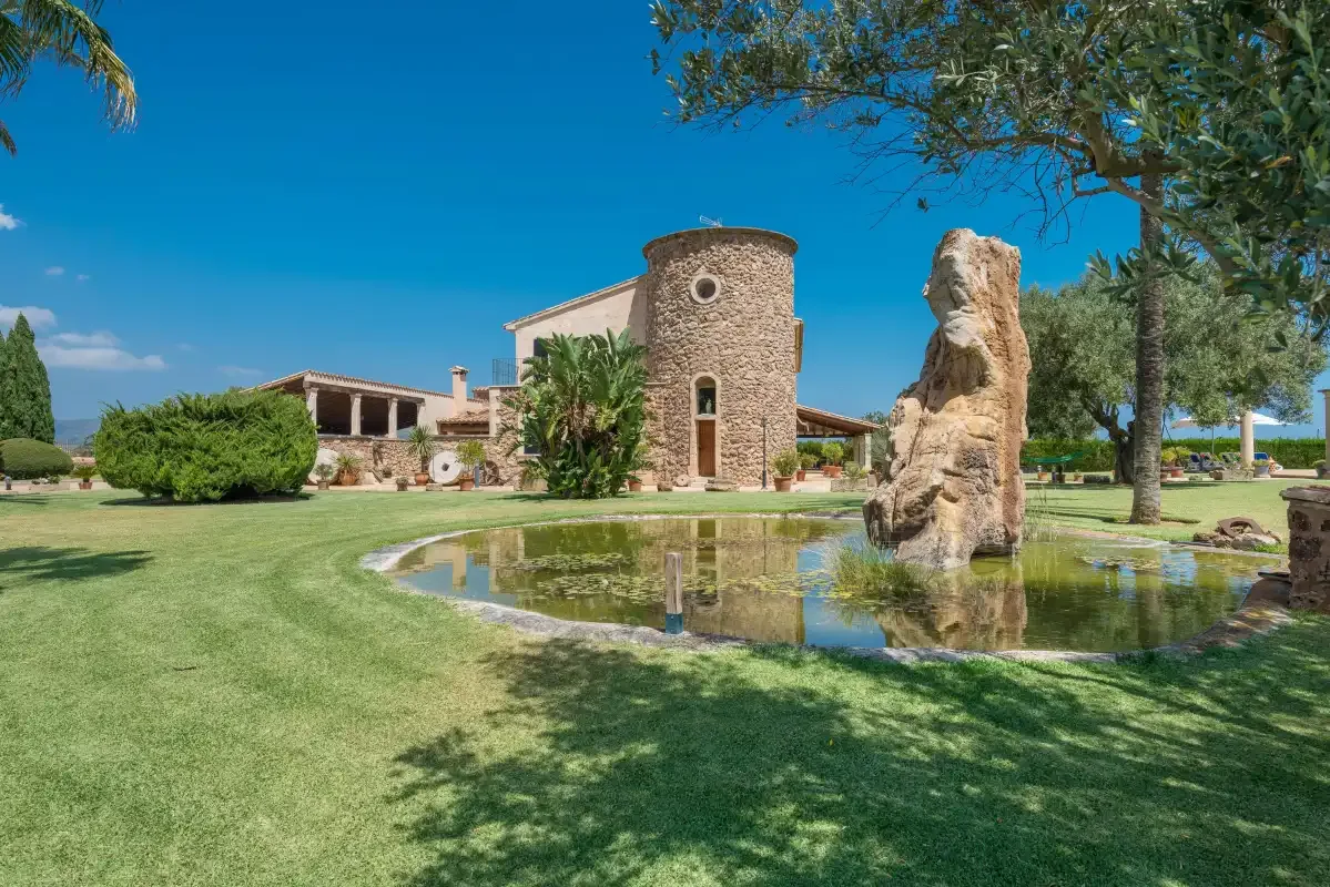 Un edificio de piedra se alza junto a un estanque reflectante en un jardín ajardinado.
