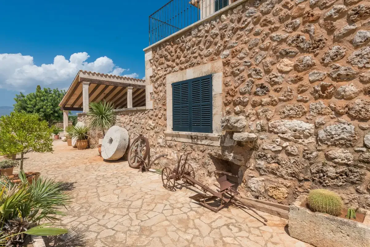 Una casa de piedra da a un patio soleado con plantas en macetas y decoración rústica.