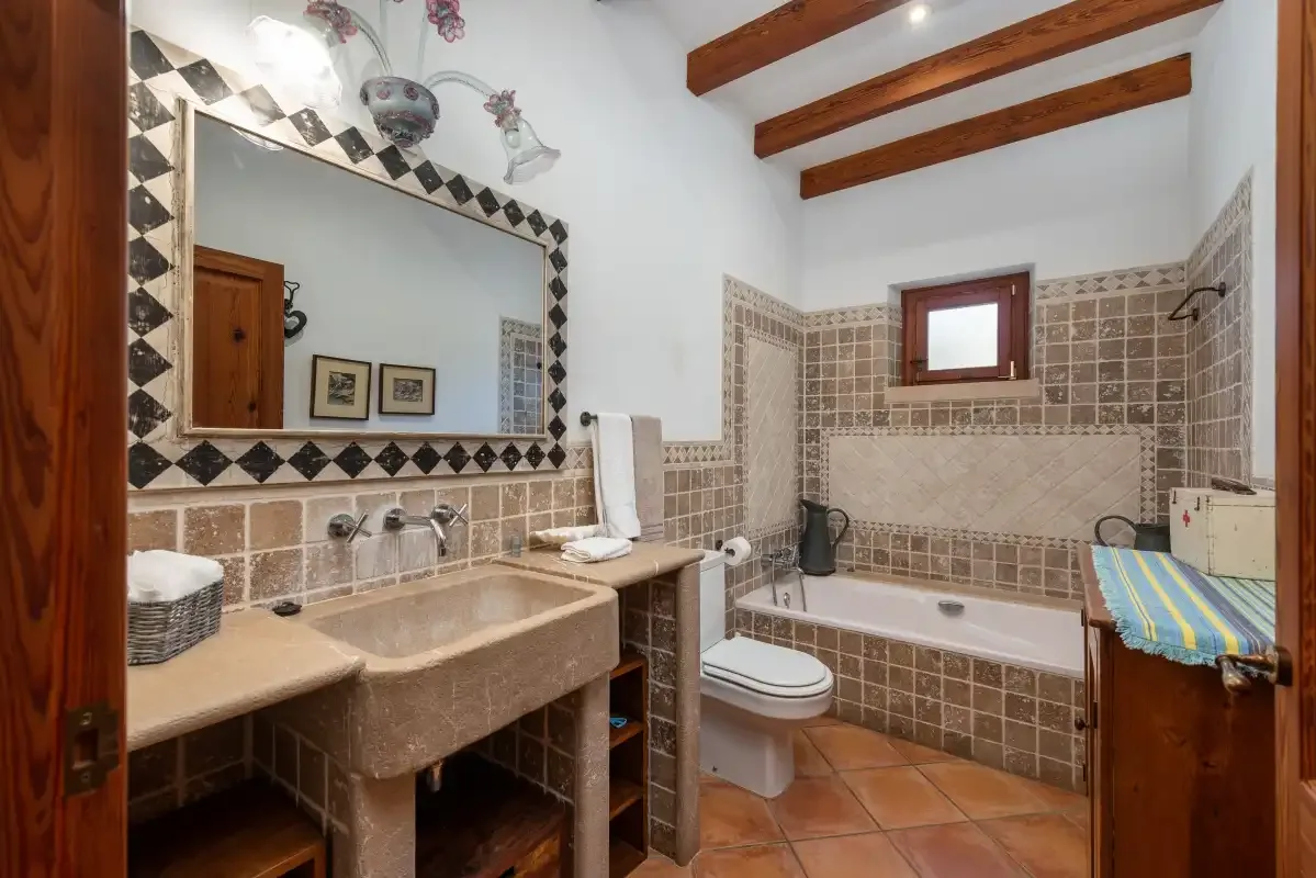 Un baño alicatado con bañera, lavabo y vigas de madera en el techo.