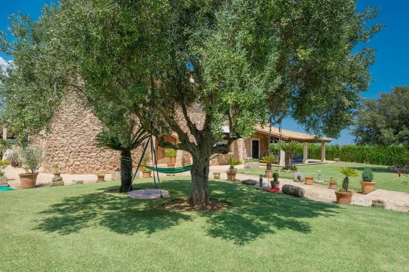Un jardín con un árbol grande, césped y un edificio de piedra al fondo.