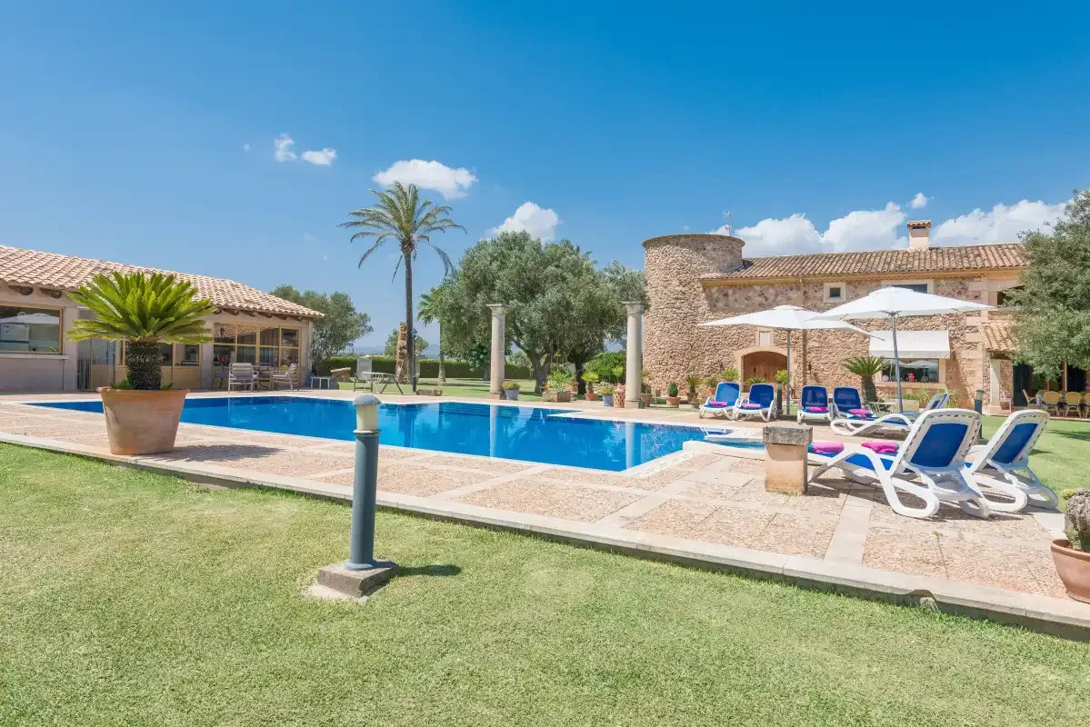Una piscina junto a un edificio de piedra, con tumbonas y césped.