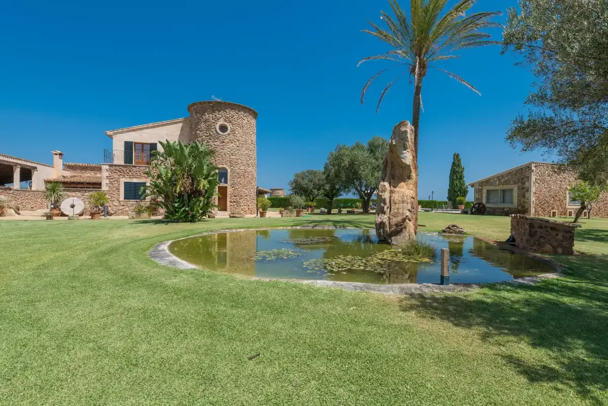 Jardines de una propiedad con un estanque, una palmera y edificios de piedra.
