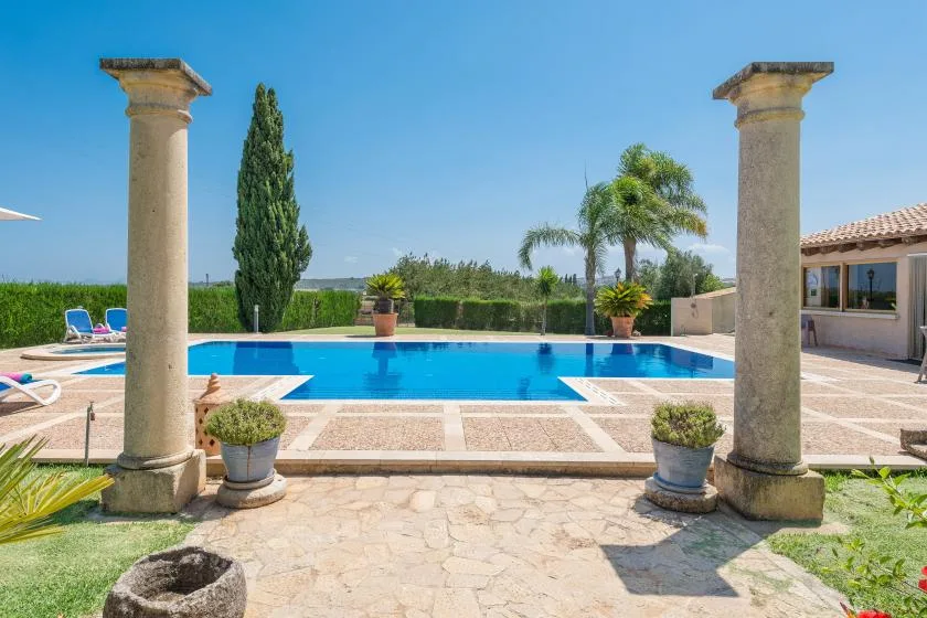 Una piscina y un patio pavimentado están enmarcados por columnas de piedra y plantas.