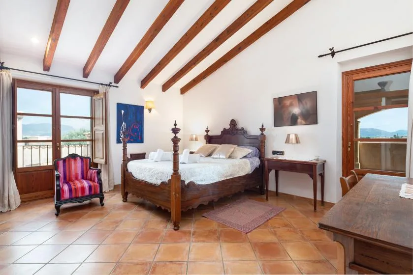 Un dormitorio con una cama de madera, un sillón colorido y vigas vistas en el techo.