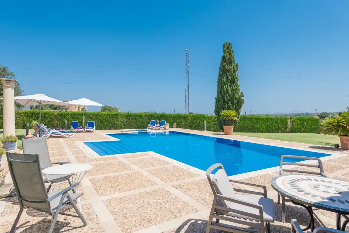 Una piscina al aire libre está rodeada de tumbonas y un patio de baldosas.