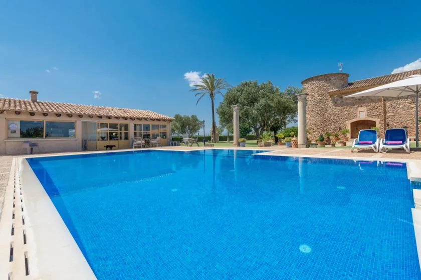Una piscina al aire libre junto a un edificio bajo y un pabellón de piedra.