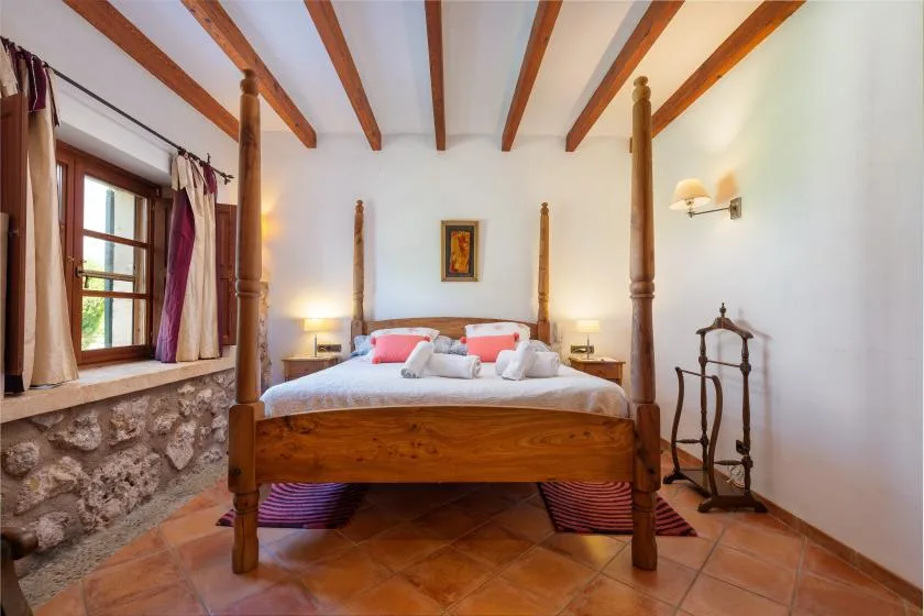 Un dormitorio con una cama con dosel de madera bajo vigas de techo expuestas.