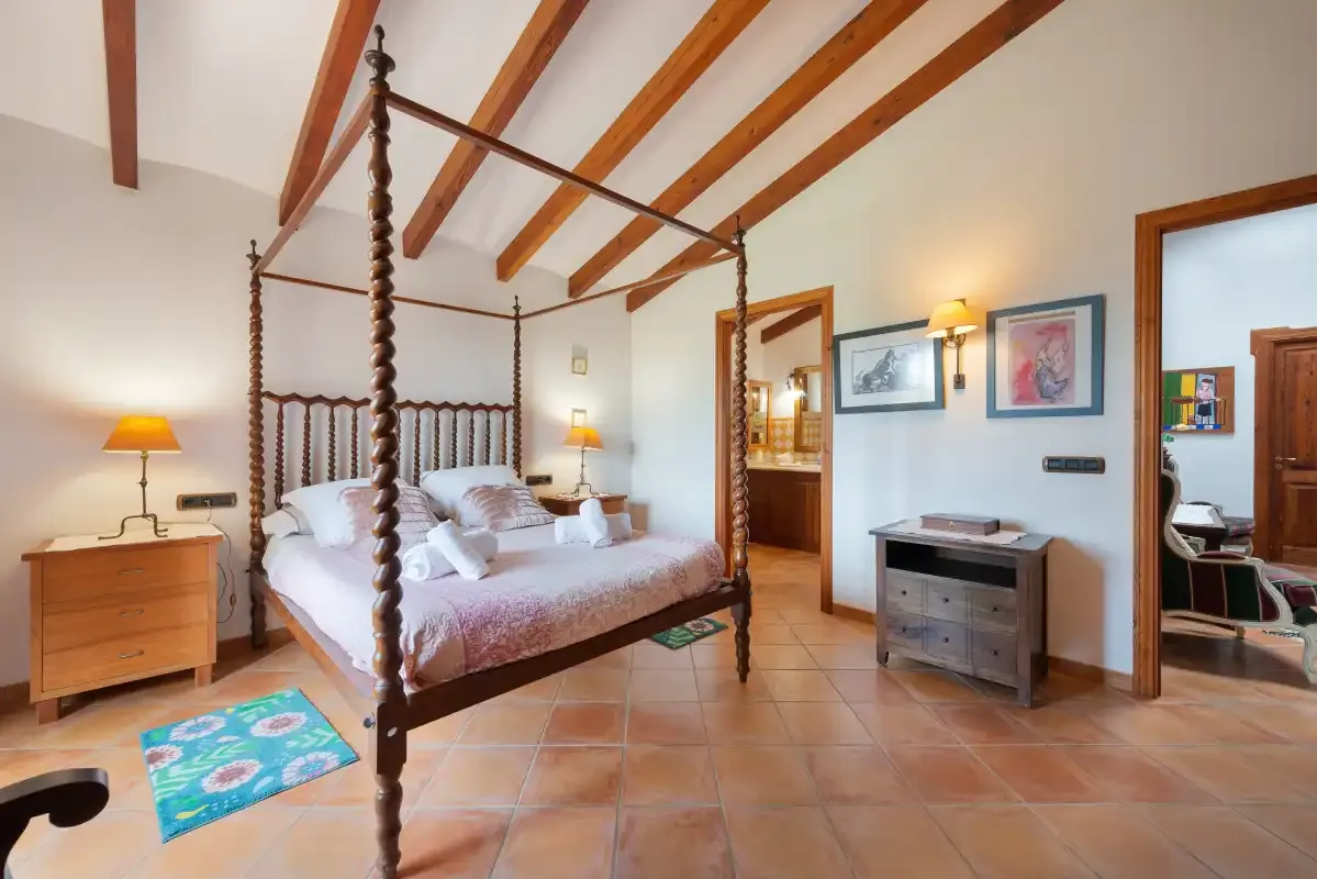 Un dormitorio con una cama con dosel, mesitas de noche y vigas vistas en el techo.