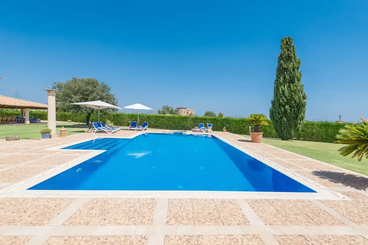 Una piscina al aire libre está rodeada por una terraza pavimentada y asientos.