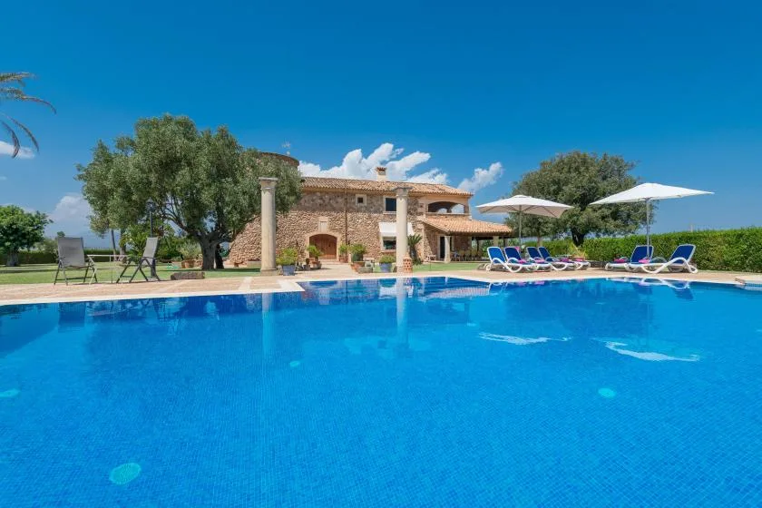 Una piscina al aire libre está junto a un edificio de piedra y tumbonas.