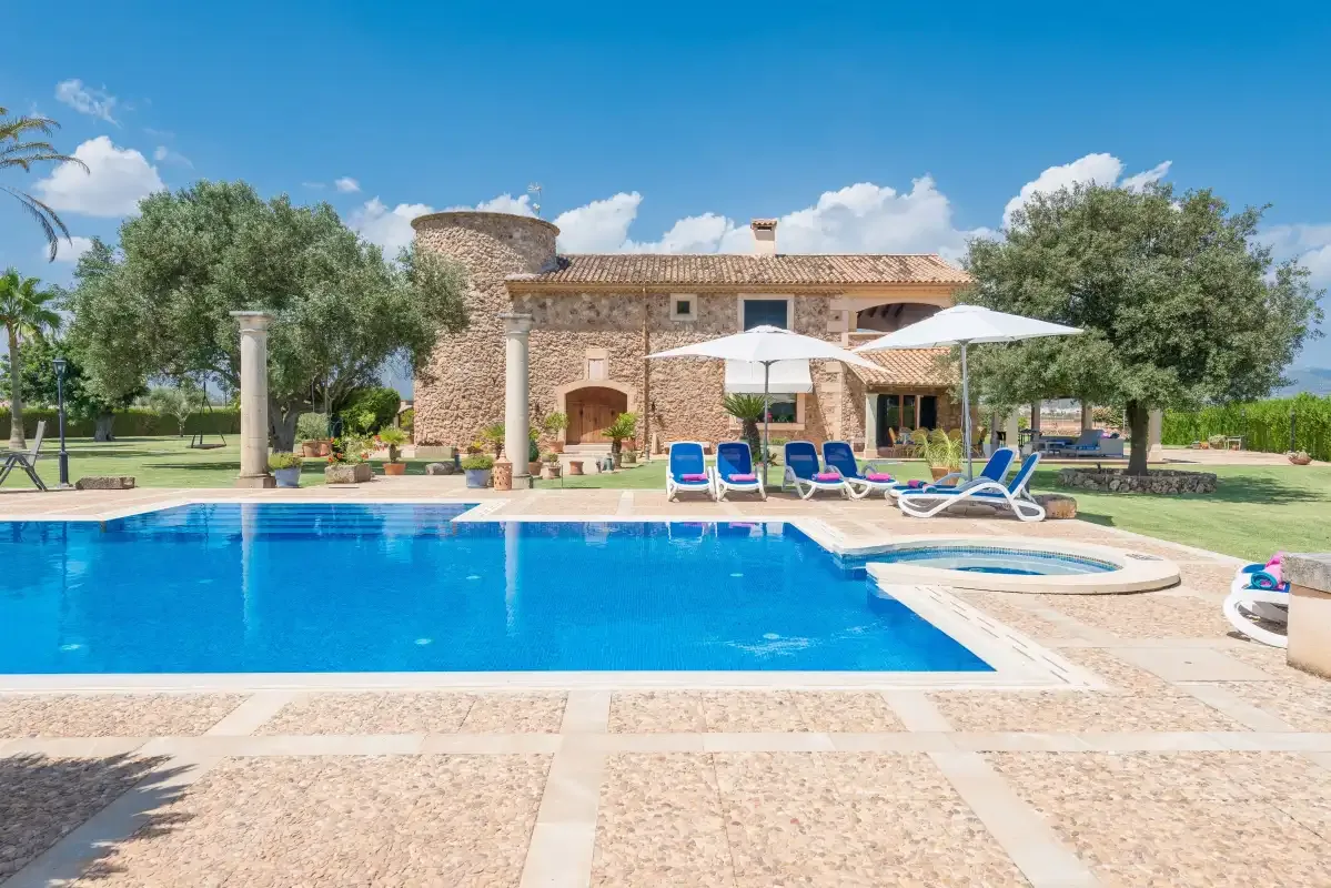 Una piscina y asientos de descanso están frente a una casa de piedra.