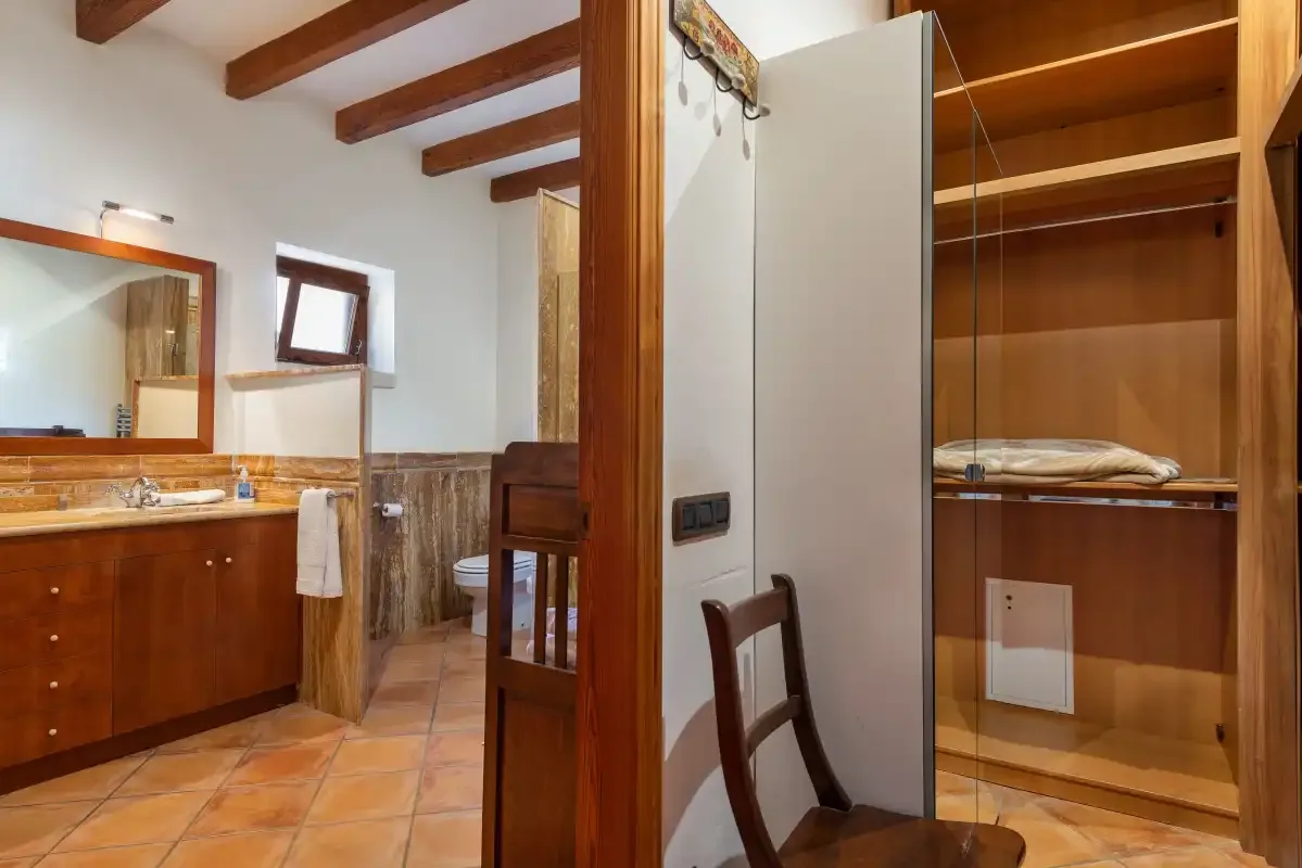 Un baño con un mueble de lavabo de madera y un armario abierto al lado.