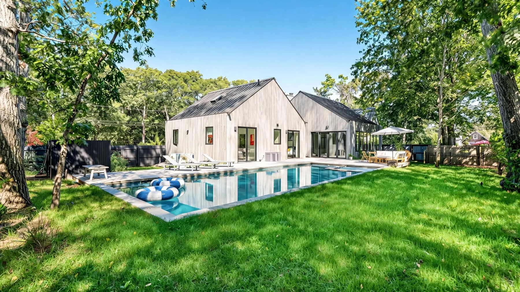 Una casa moderna da a una piscina en un jardín verde y arbolado.