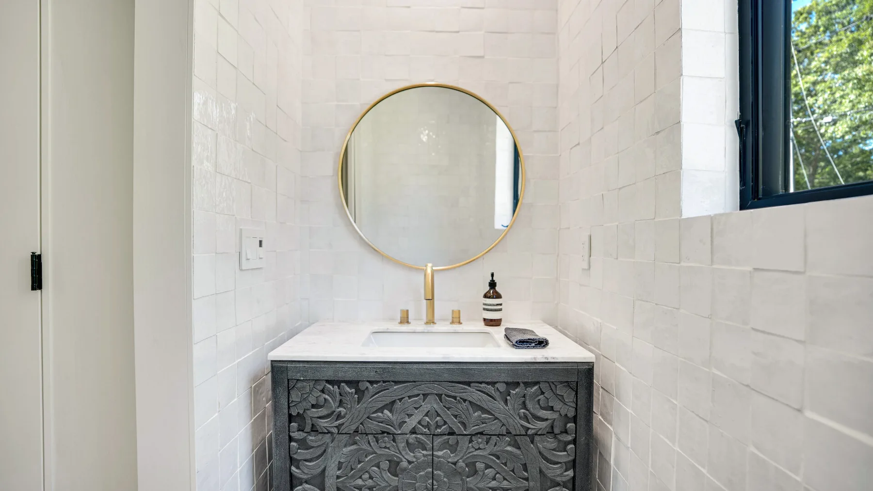 Un tocador de baño con espejo redondo y un mueble oscuro decorativo.