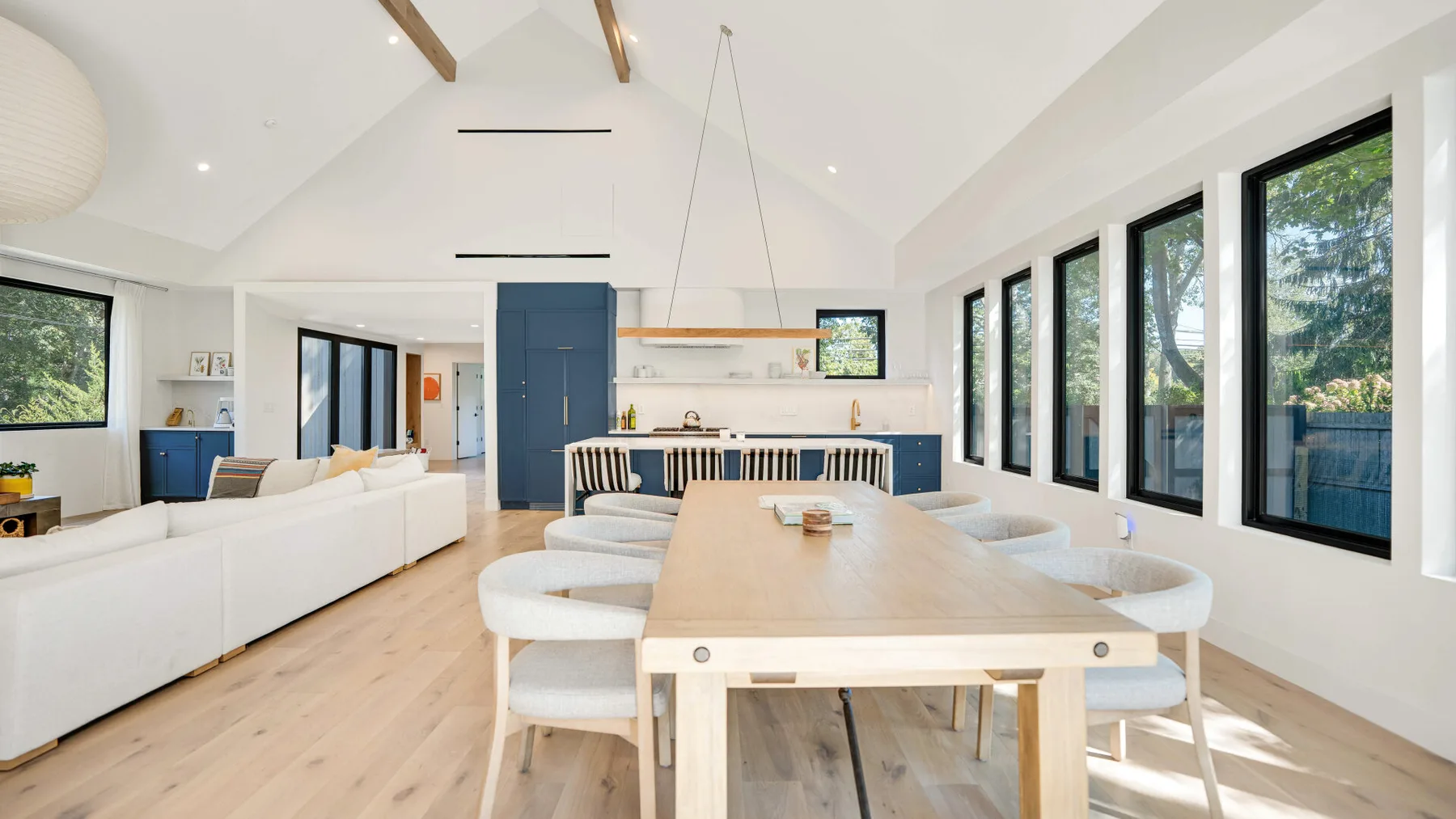 Una luminosa sala-comedor de concepto abierto tiene asientos blancos y una mesa larga de madera.