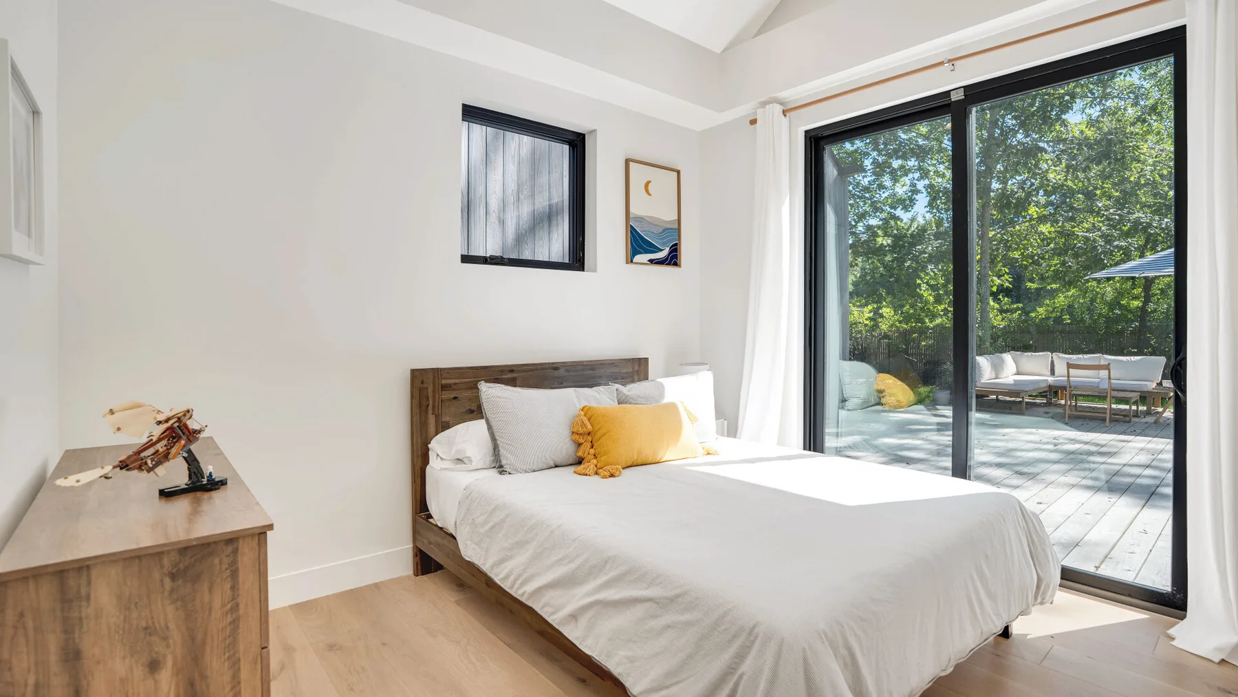 Un dormitorio luminoso con una cama tendida junto a grandes puertas de vidrio que dan a un patio.