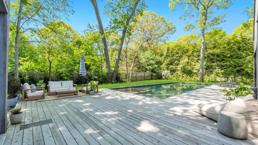 Una piscina al aire libre rodeada de árboles está junto a una amplia terraza de madera con asientos.