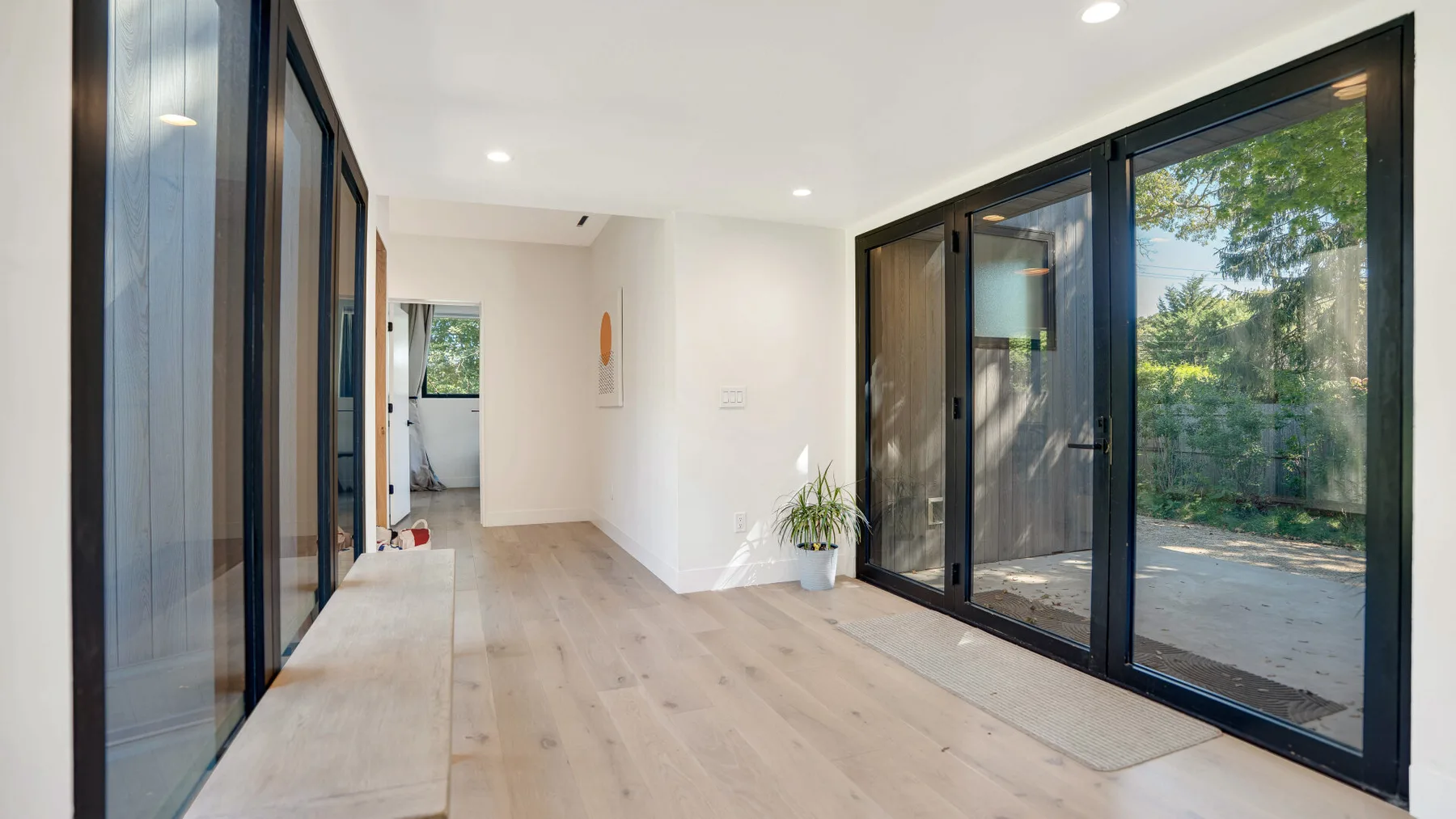 Una habitación luminosa con suelo claro y grandes puertas de vidrio frente a la vegetación.