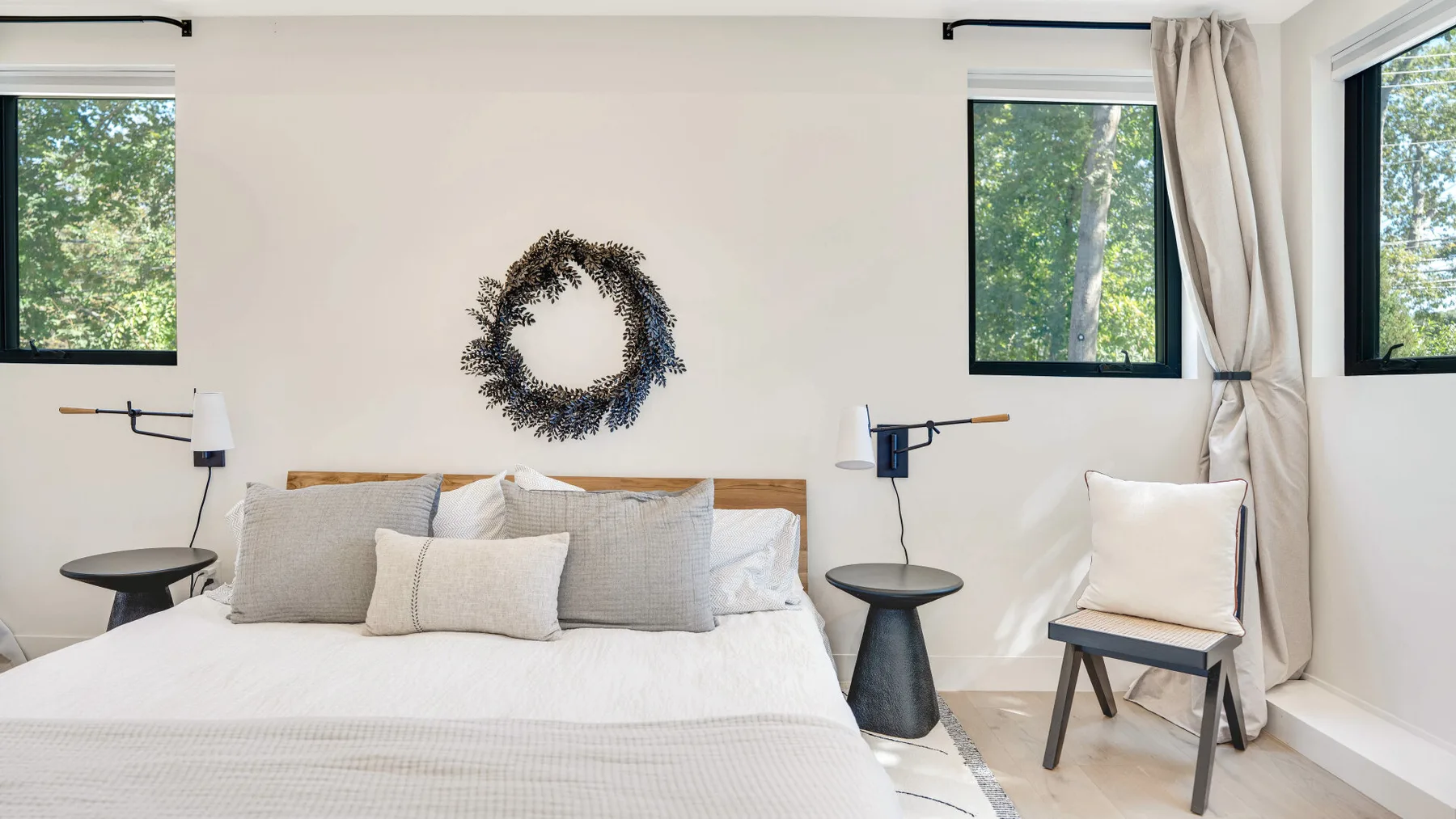 Un dormitorio luminoso con una cama, luces de lectura en la pared y ventanas con vistas a la vegetación.