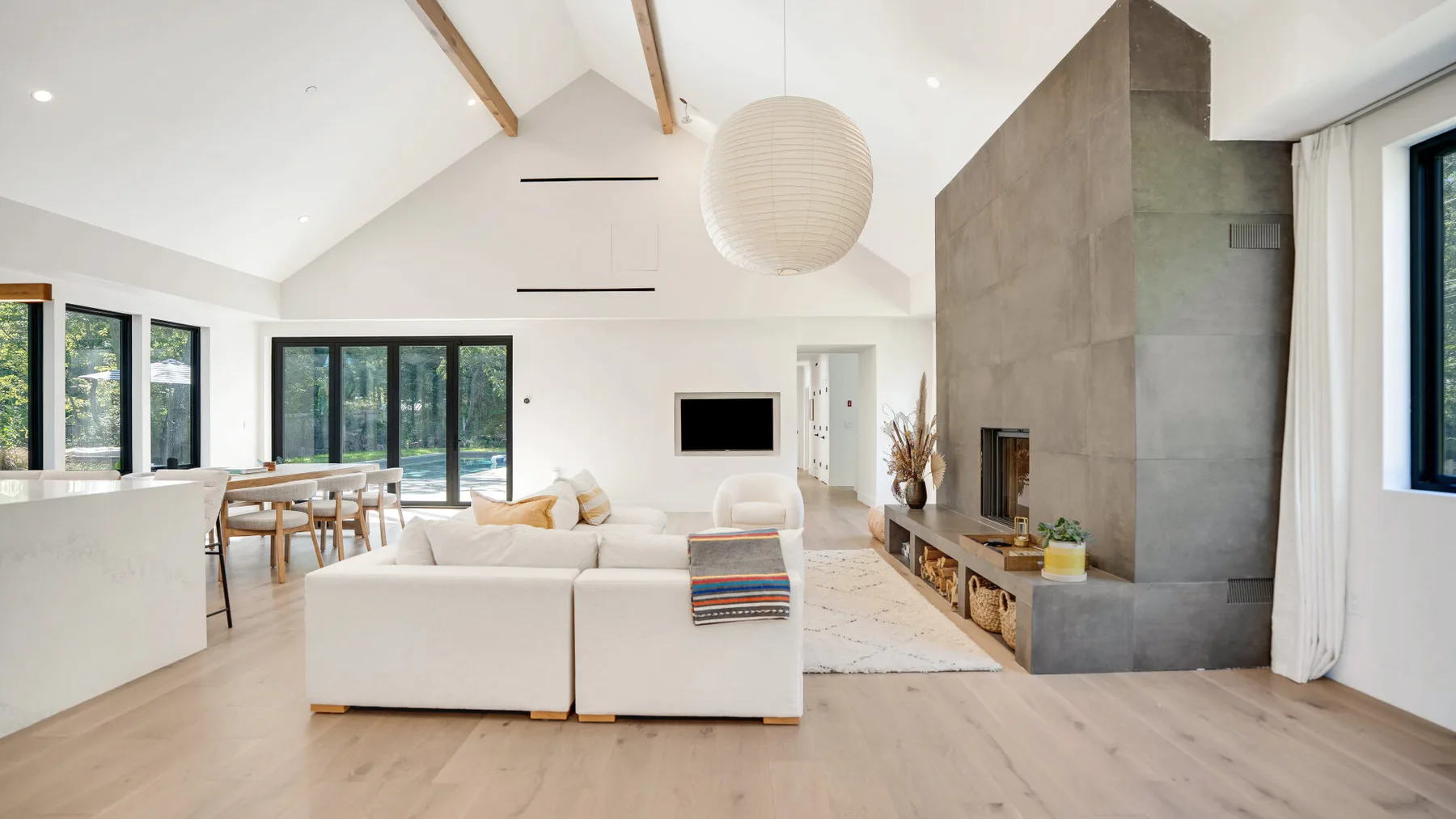 Luminoso salón de planta abierta con zona de estar, comedor y una chimenea alta.