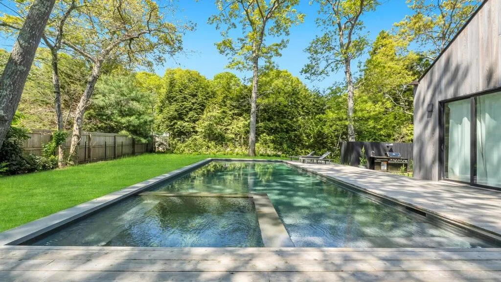 Una piscina en el patio, junto a un césped verde, árboles y un edificio moderno.